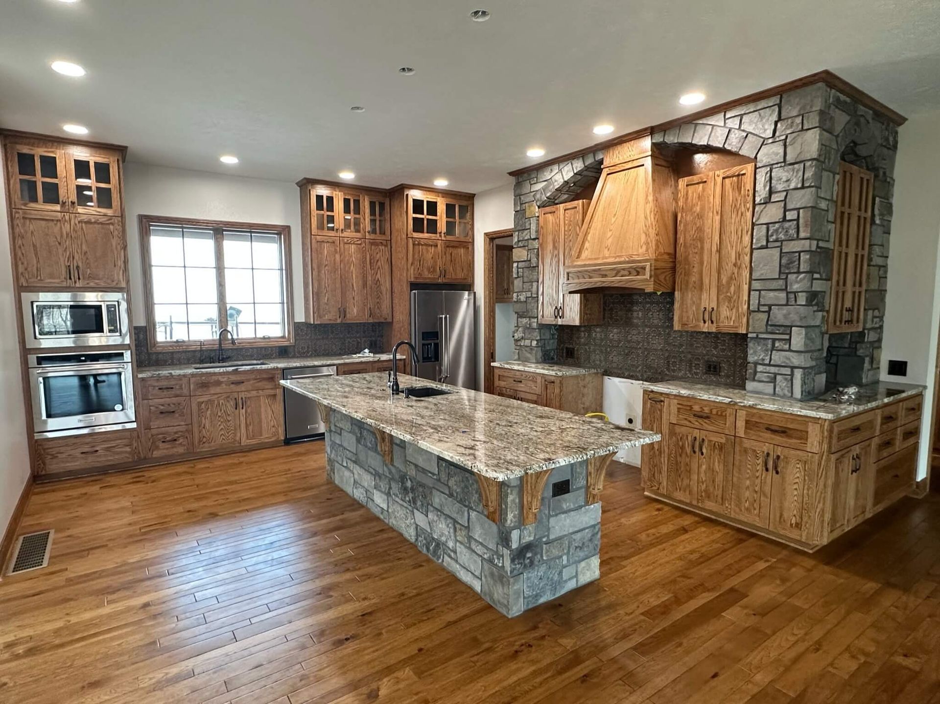 A kitchen with oak cabinets, granite countertops, a large stone-covered island, and hardwood floors.