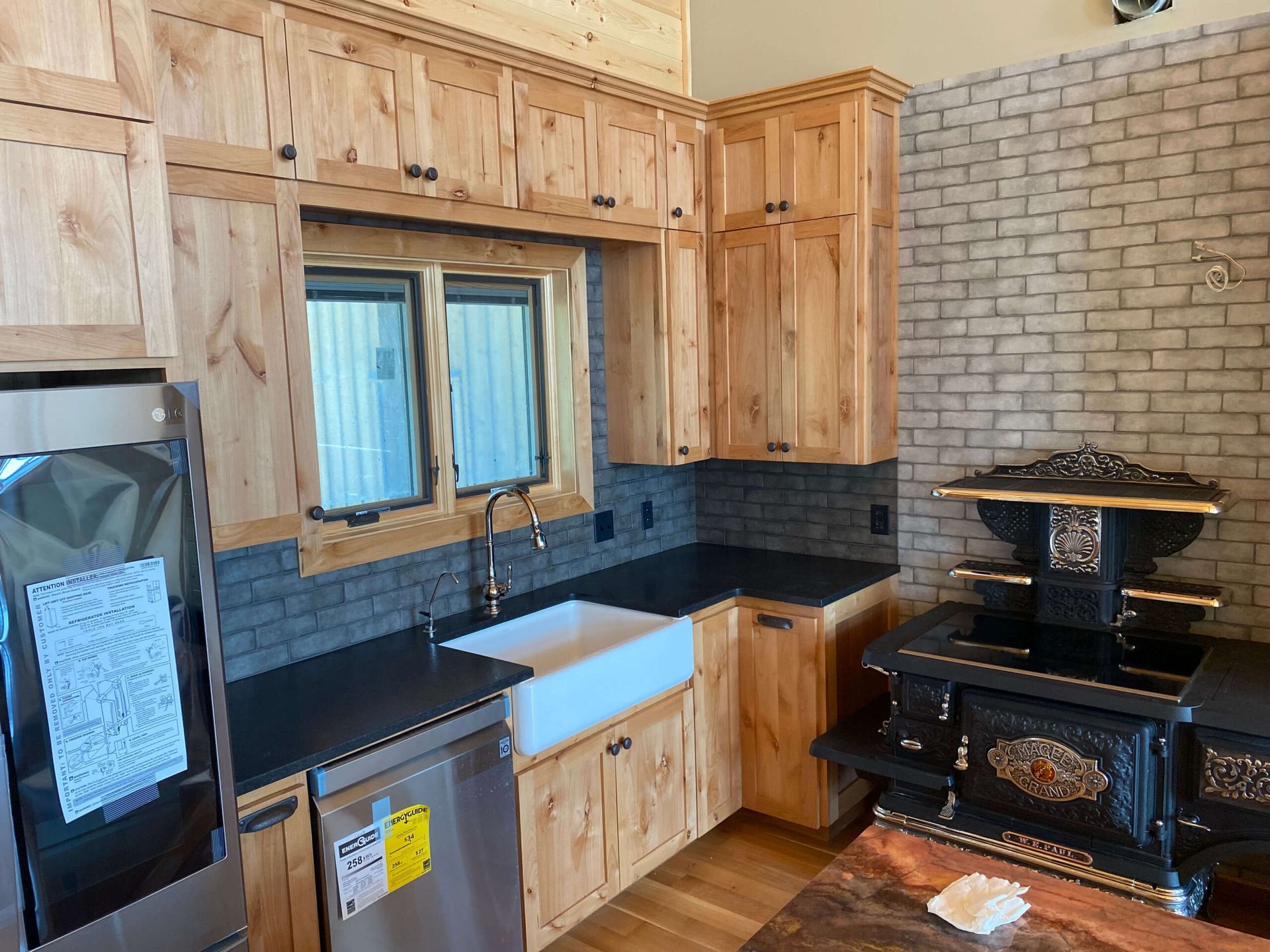 A kitchen featuring wood cabinets, dark counters, a white farmhouse sink, and a vintage-style black wood-burning stove.