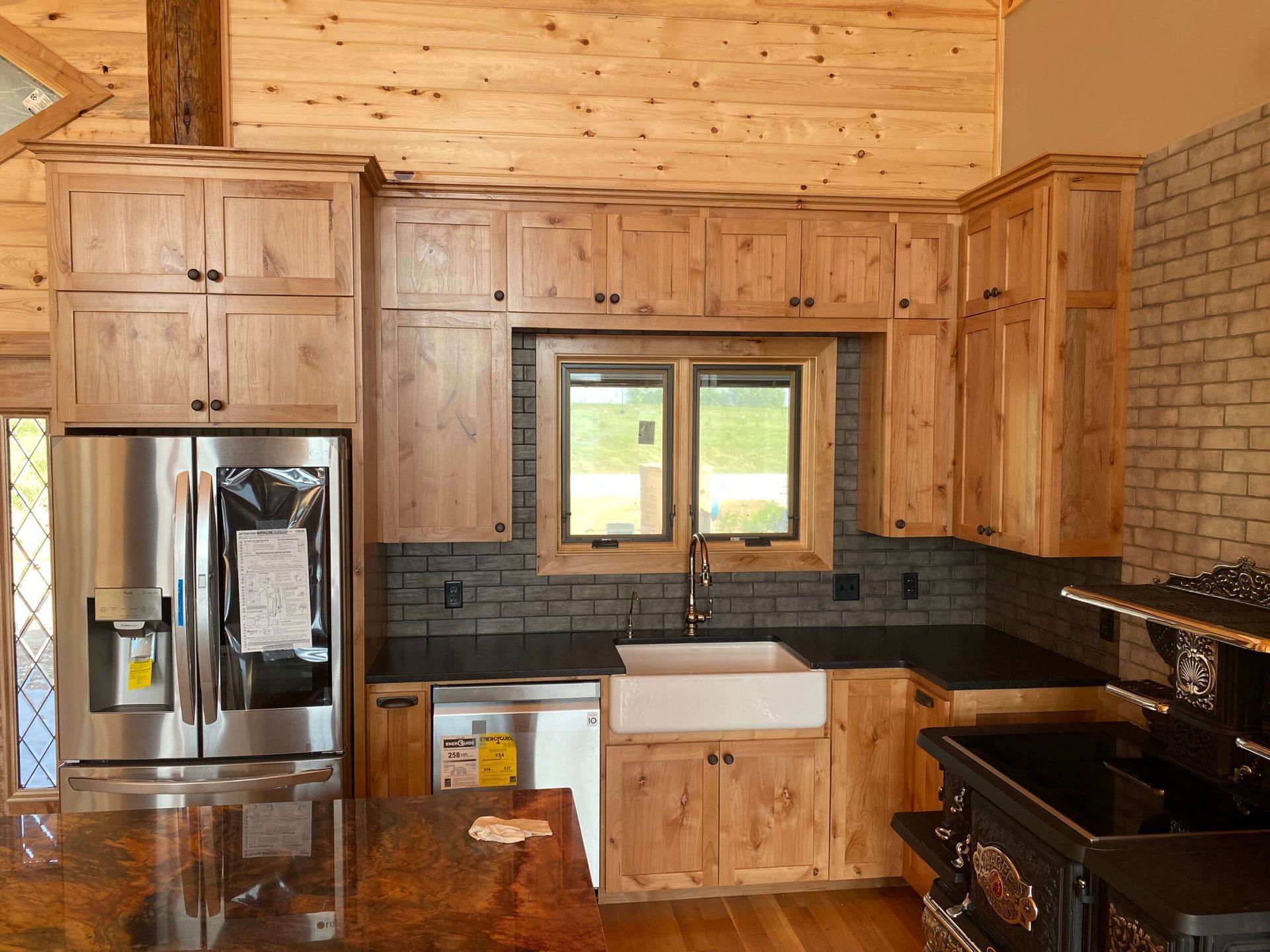 A kitchen featuring rustic wood cabinets, a farmhouse sink, stainless steel refrigerator, and dark granite countertops.