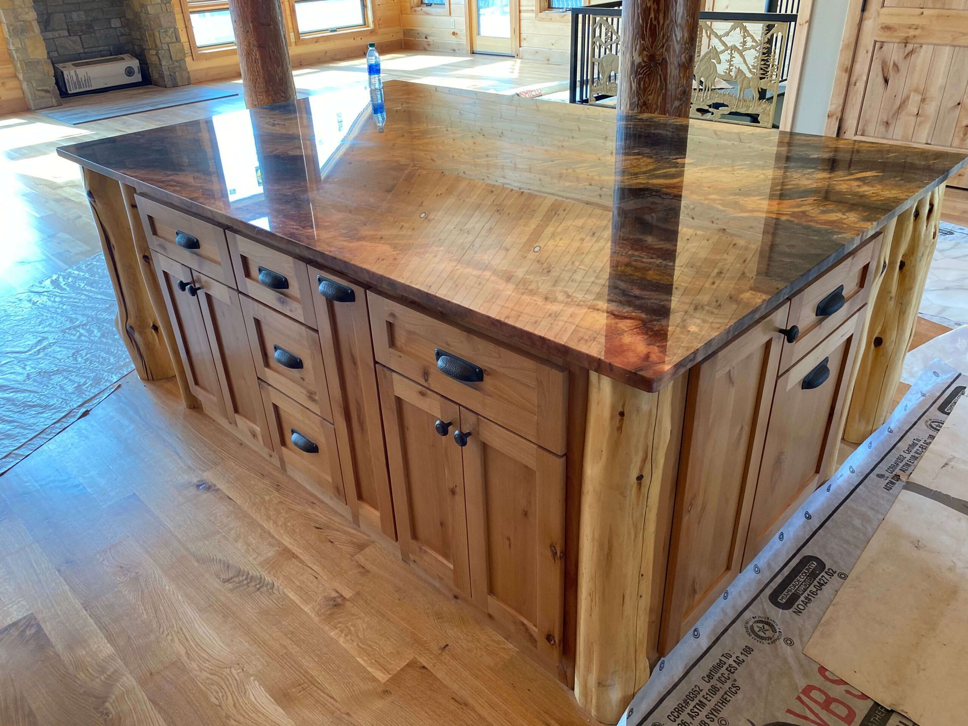 A wooden kitchen island with a dark, polished stone countertop in a rustic-style room with hardwood flooring.