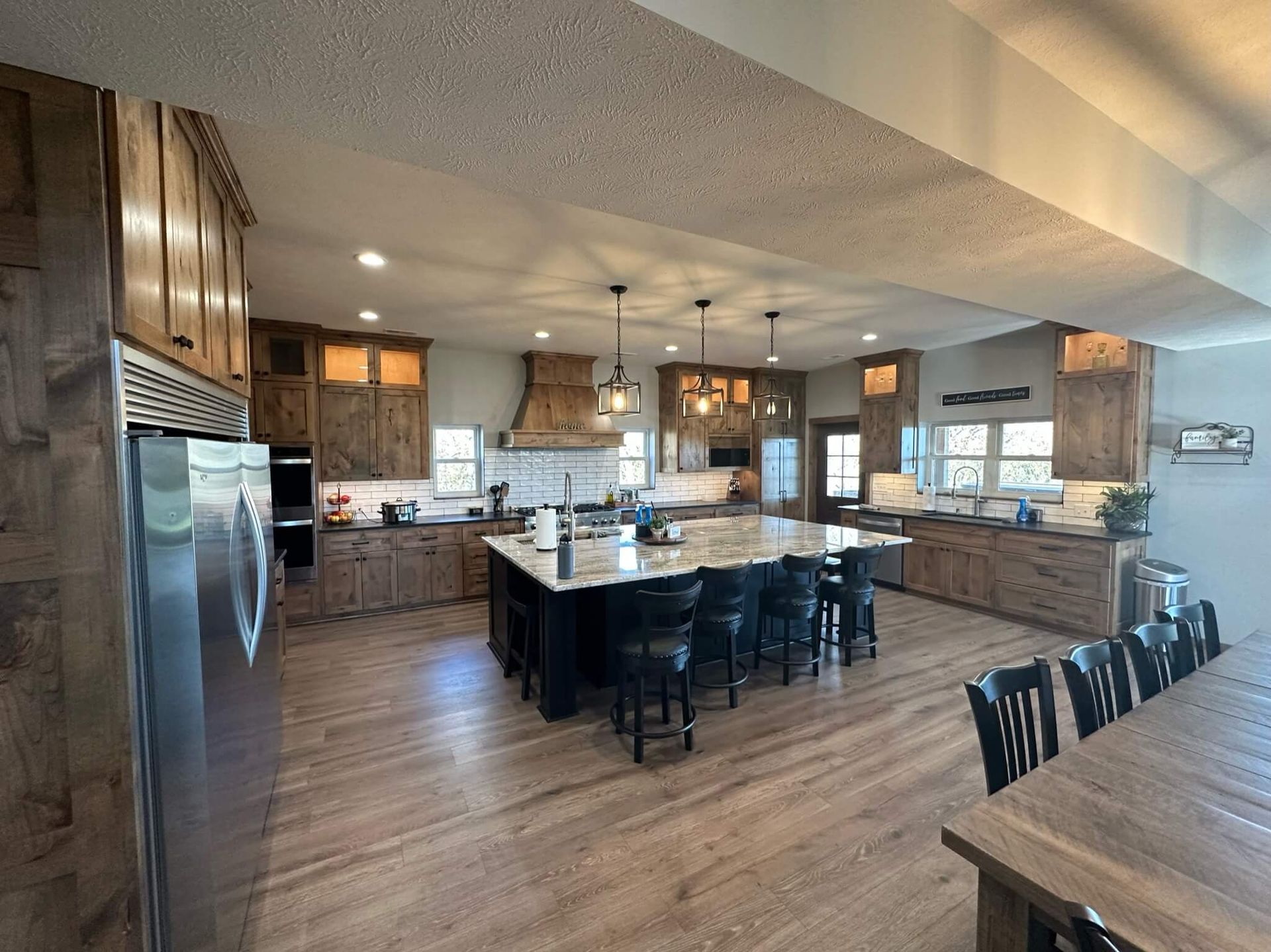 Spacious kitchen with wood cabinets, a large granite-topped island, bar stools, and warm wood flooring.