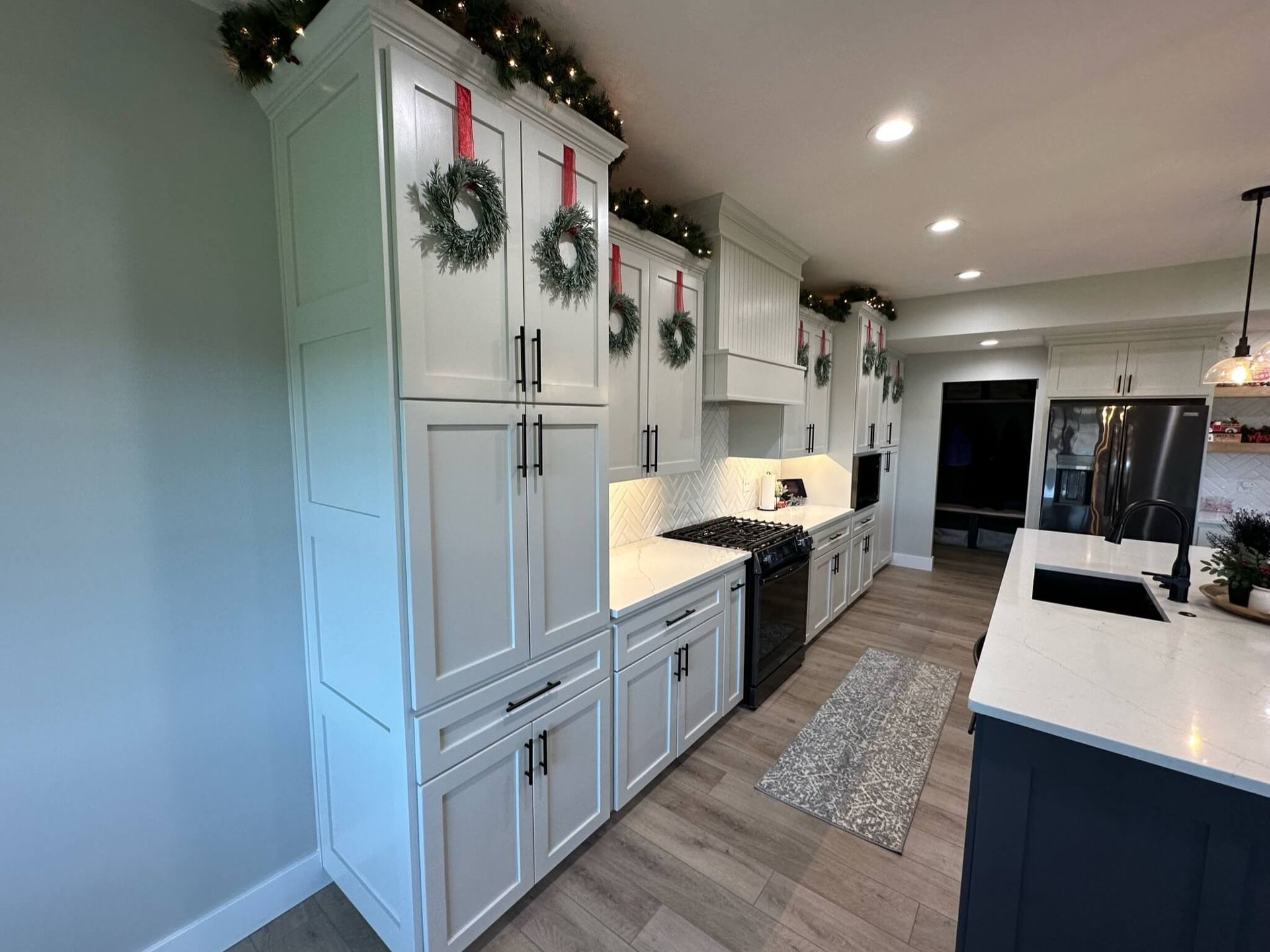 A modern kitchen with white cabinets, dark island, stainless steel appliances, and festive greenery decor.