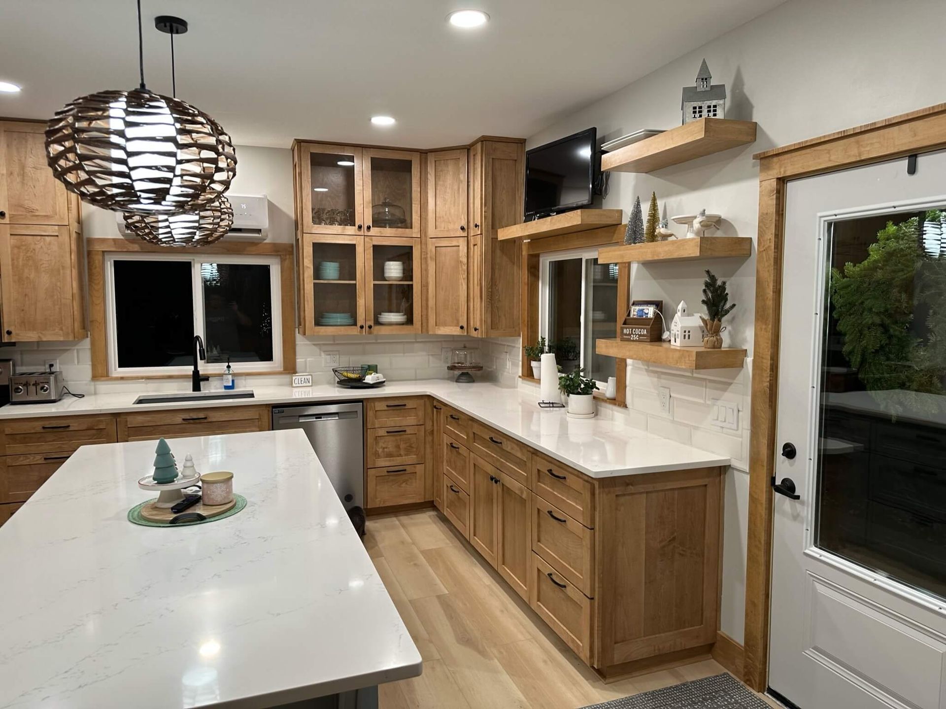 A kitchen with light wood cabinets, white countertops, an island, open shelving, and two large, textured pendant lights.