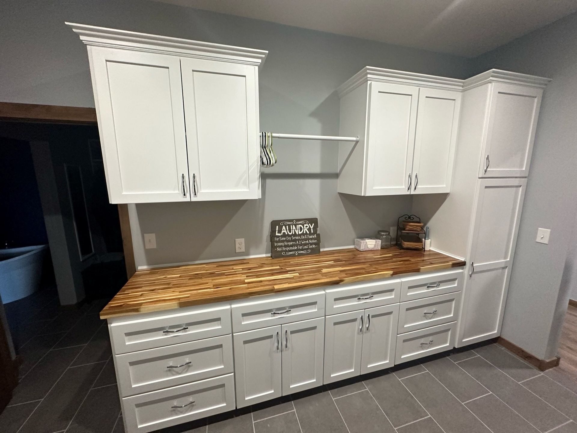 White kitchen cabinets with a butcher block countertop and gray floor tiles in a home interior.