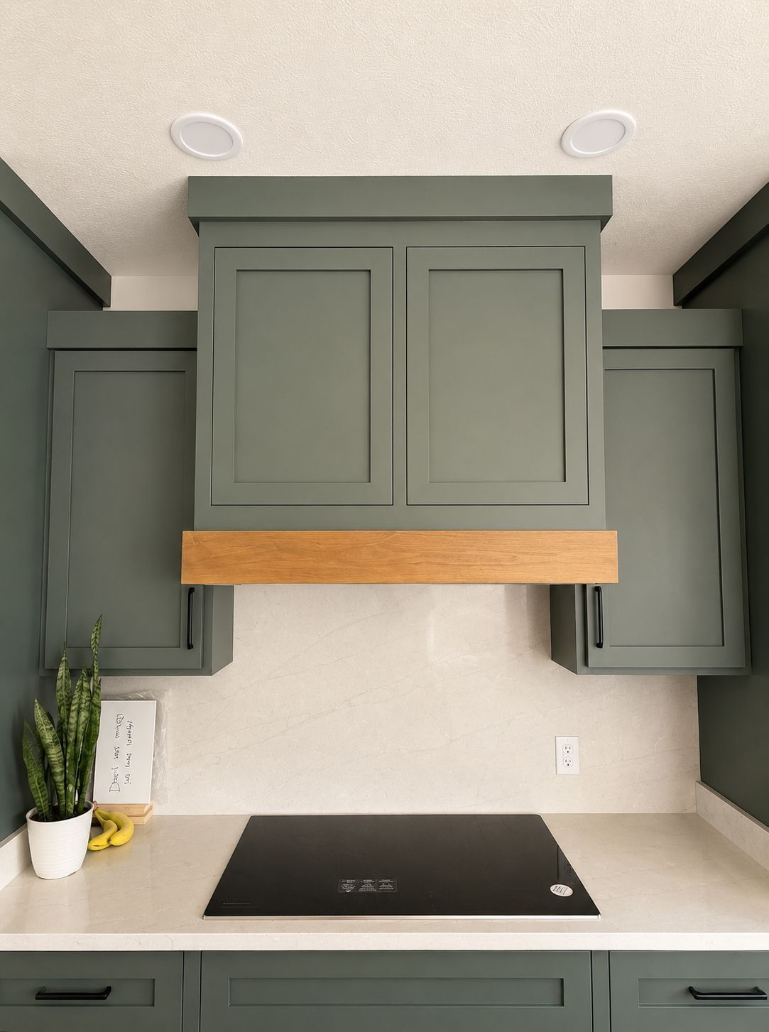 Blue-gray kitchen cabinets with a wood range hood over a beige countertop and black cooktop