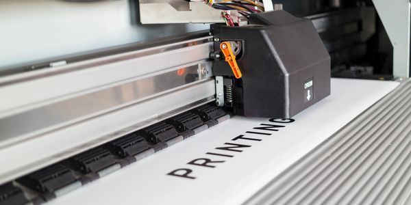 A printing factory interior with large printing machines, rolls of paper, and printed sheets.