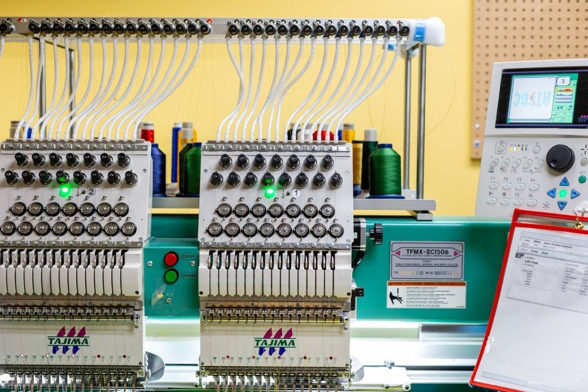 Two industrial embroidery machines with multiple spools of thread and control panel.
