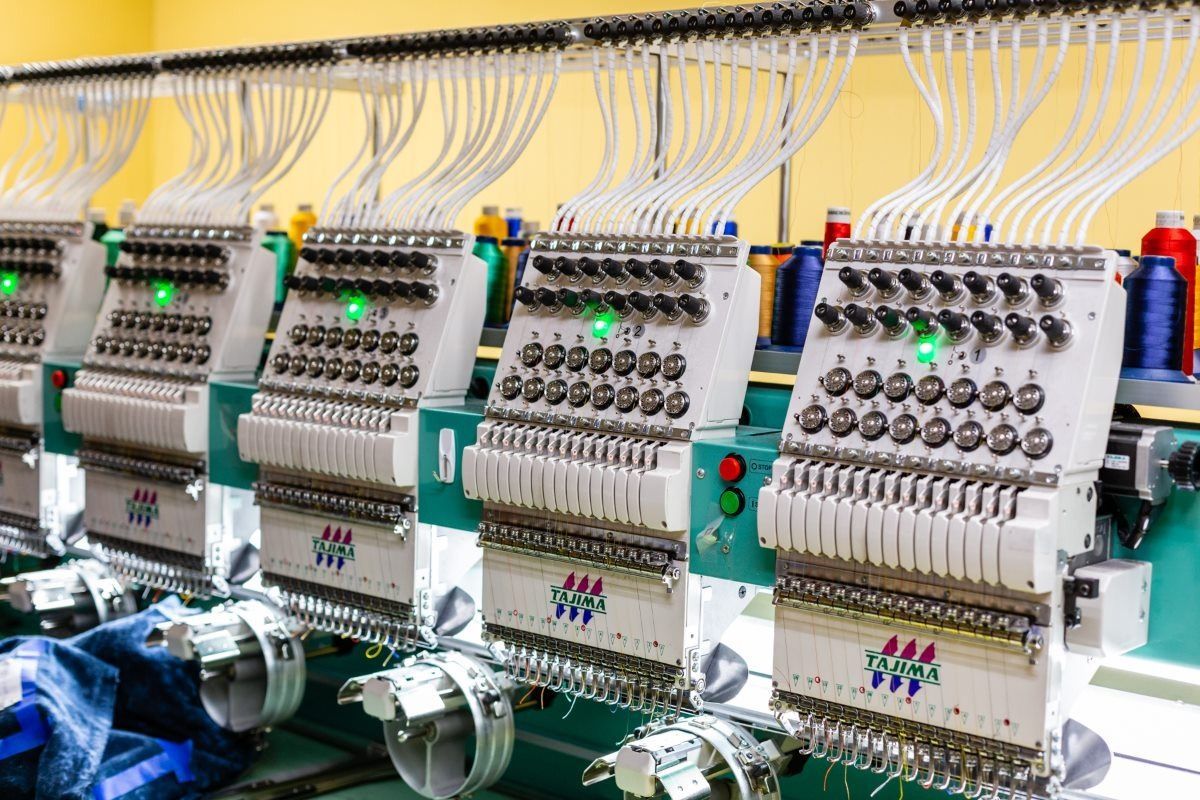 Row of industrial embroidery machines with spools of thread.