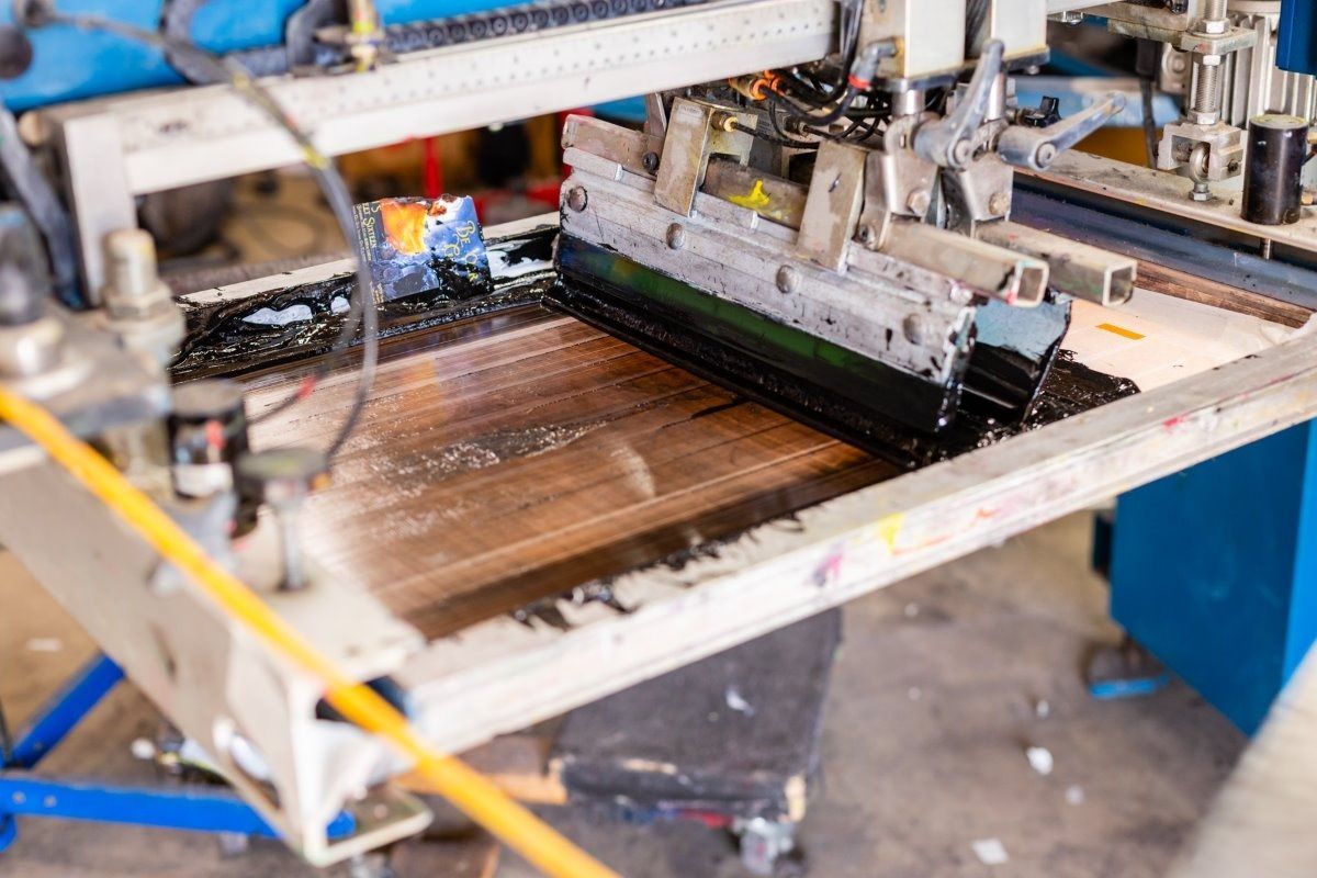 Screen printing machine in operation, with black ink on a wooden surface.