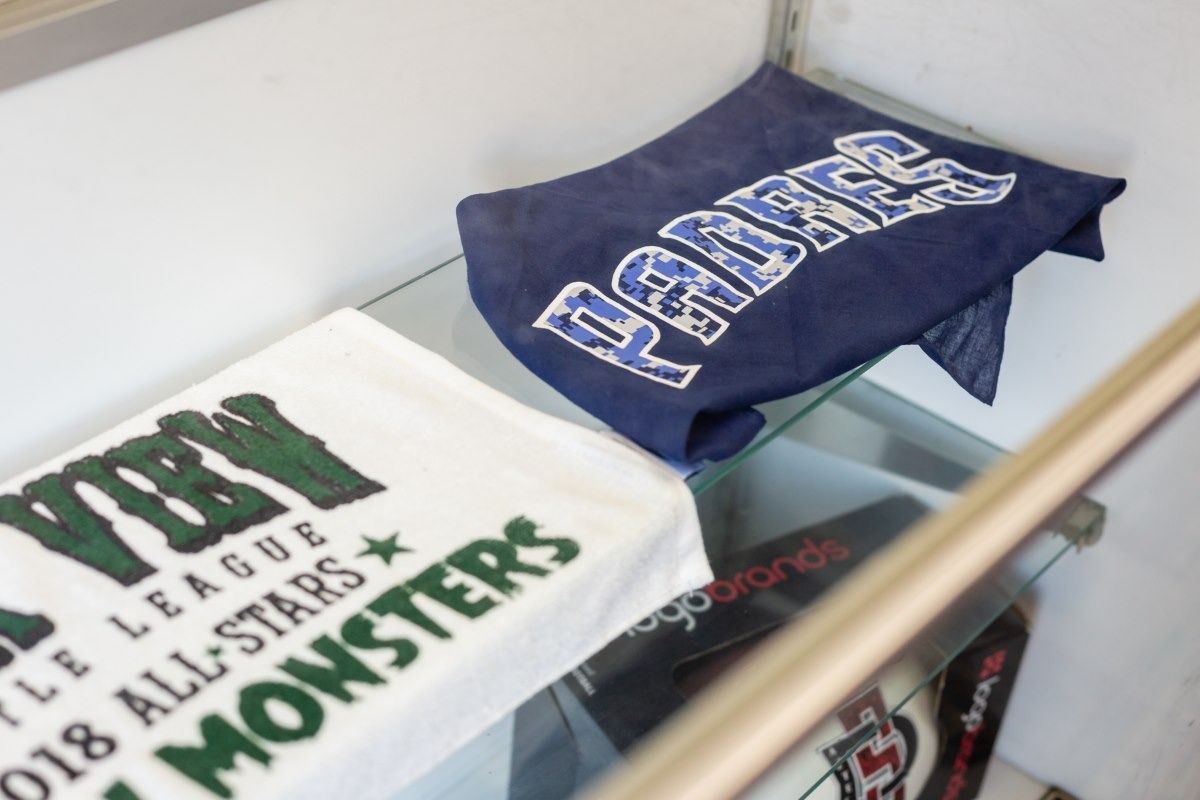Two towels on a glass shelf. One white with green text, another blue with white text.