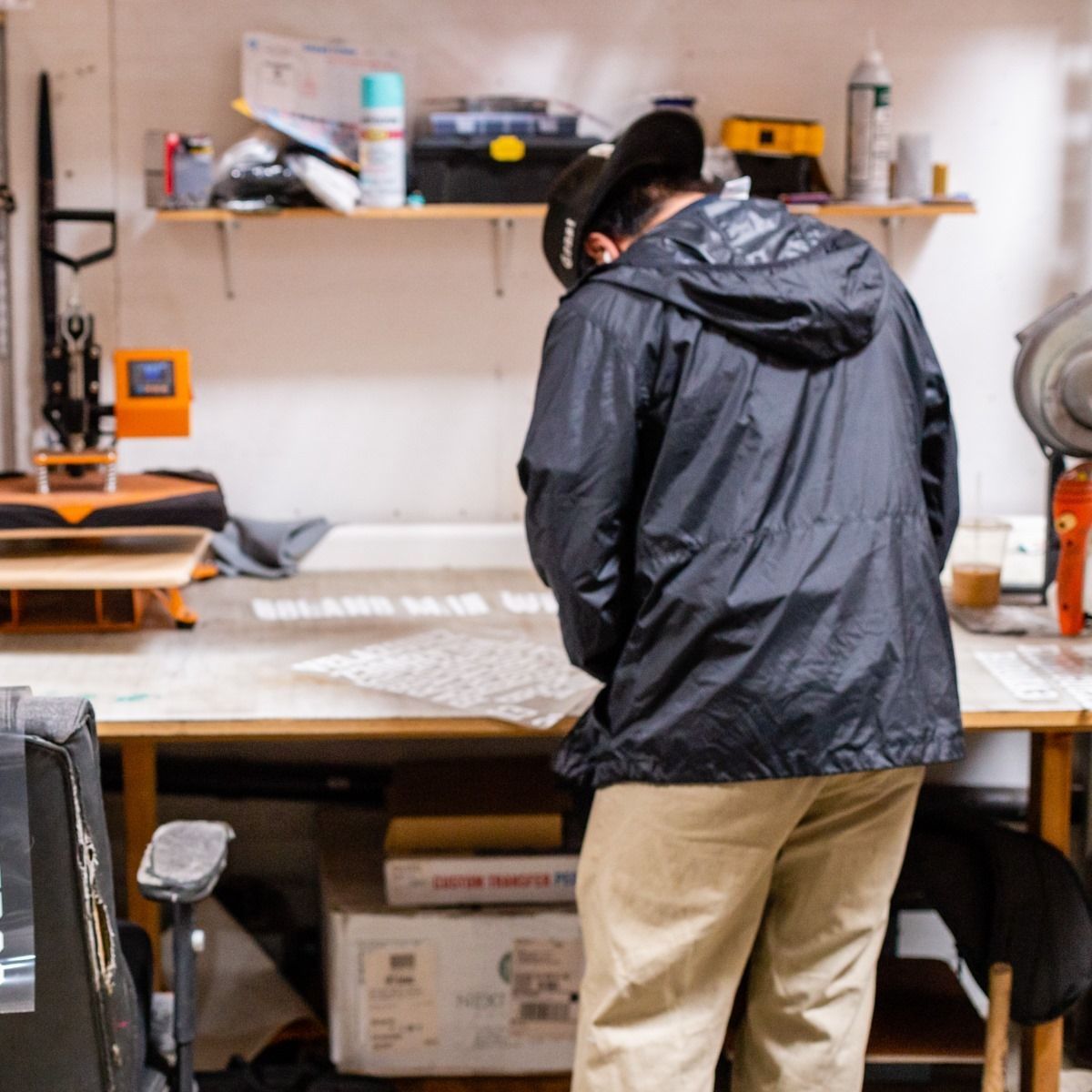 Person in black jacket looking at paper on a work table in a workshop.