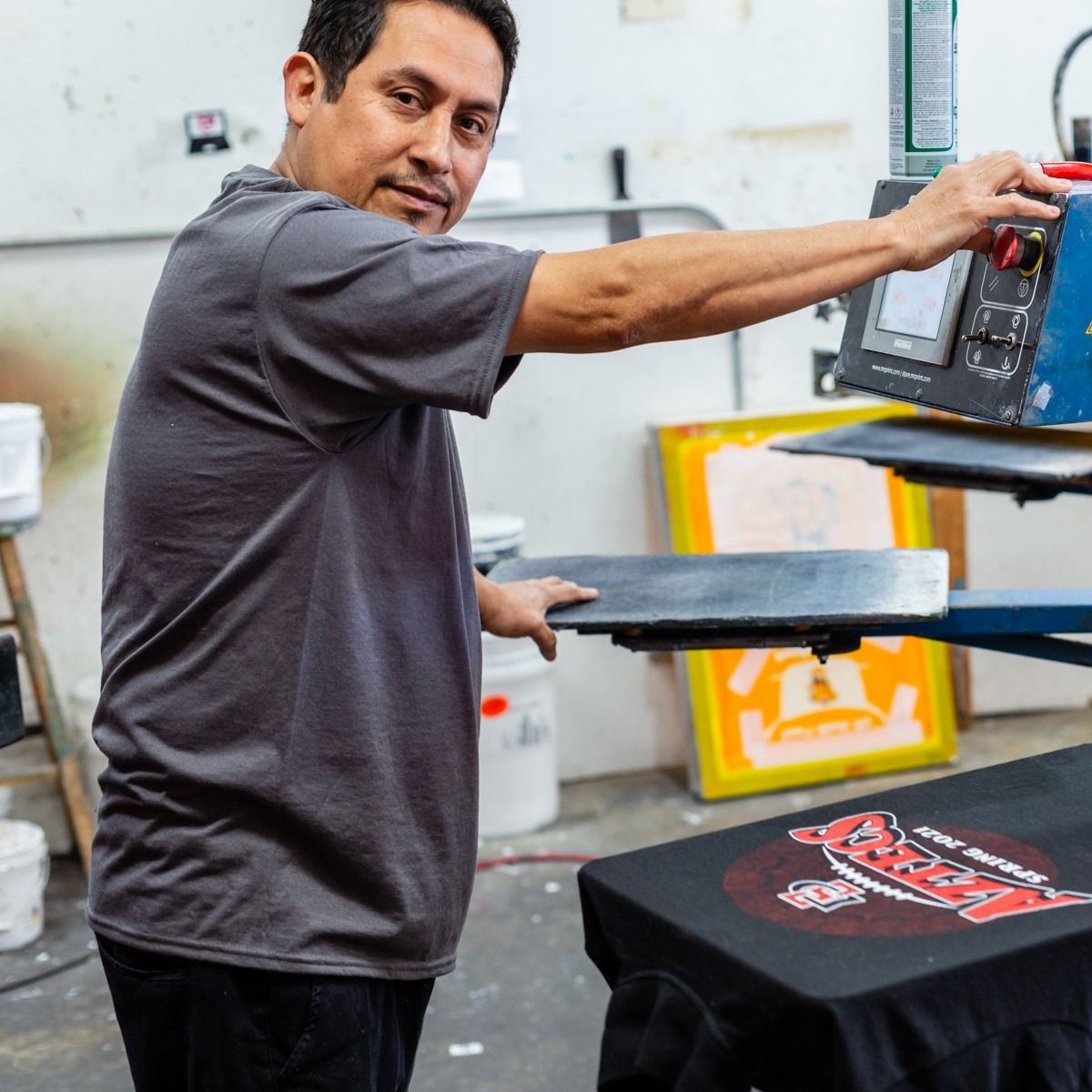 Man printing a design on a black t-shirt using a screen printing machine.
