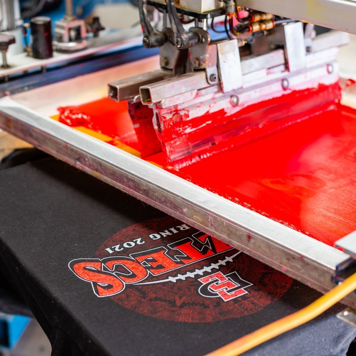 Screen printing machine applying red ink to a black t-shirt with a logo.