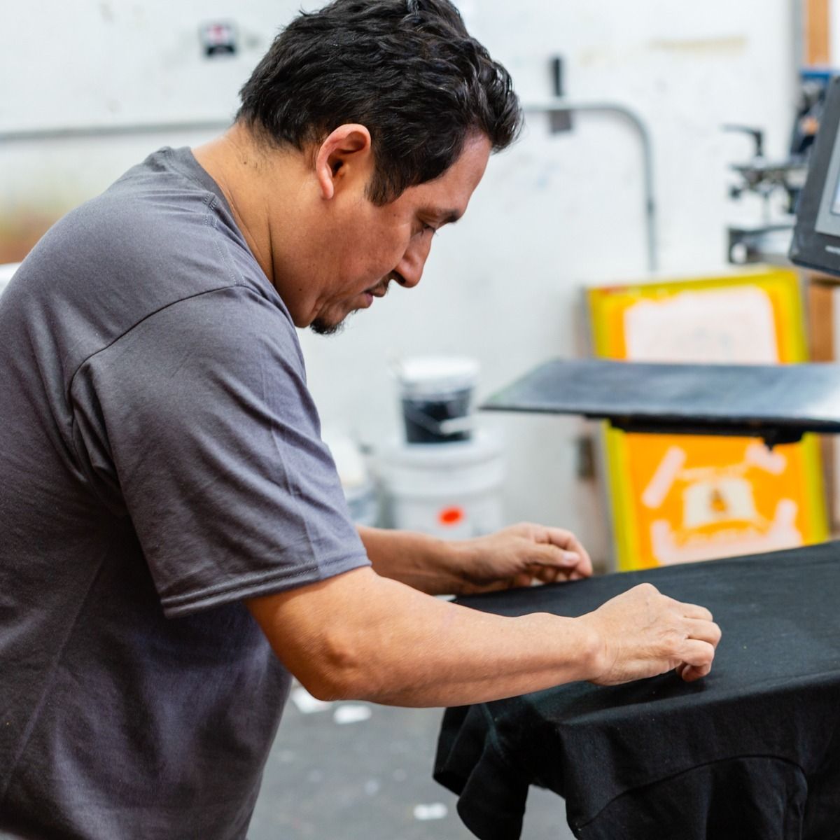 Man wearing gray shirt printing on a black t-shirt in a workshop.