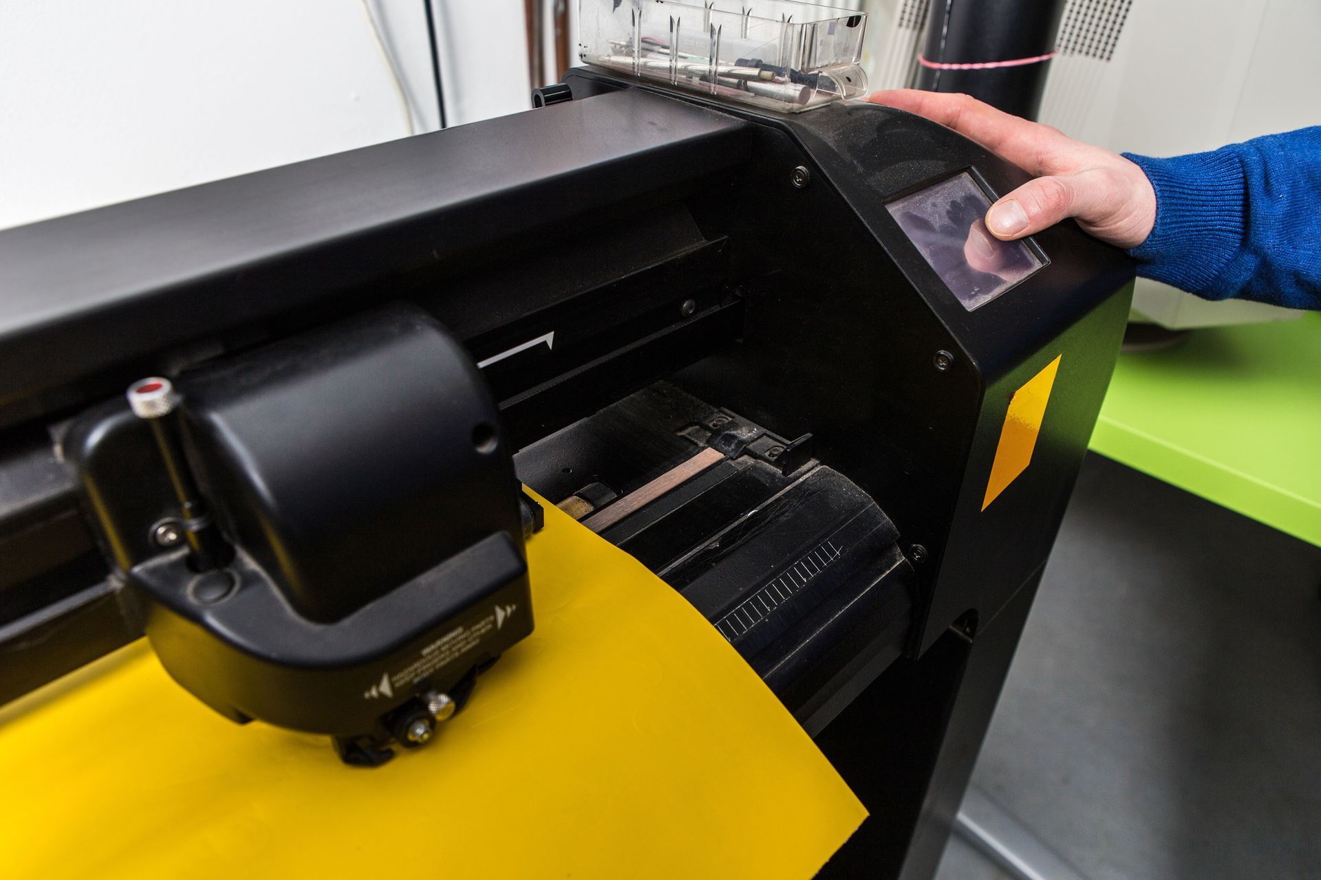 Person operating a black vinyl cutting machine with yellow material.