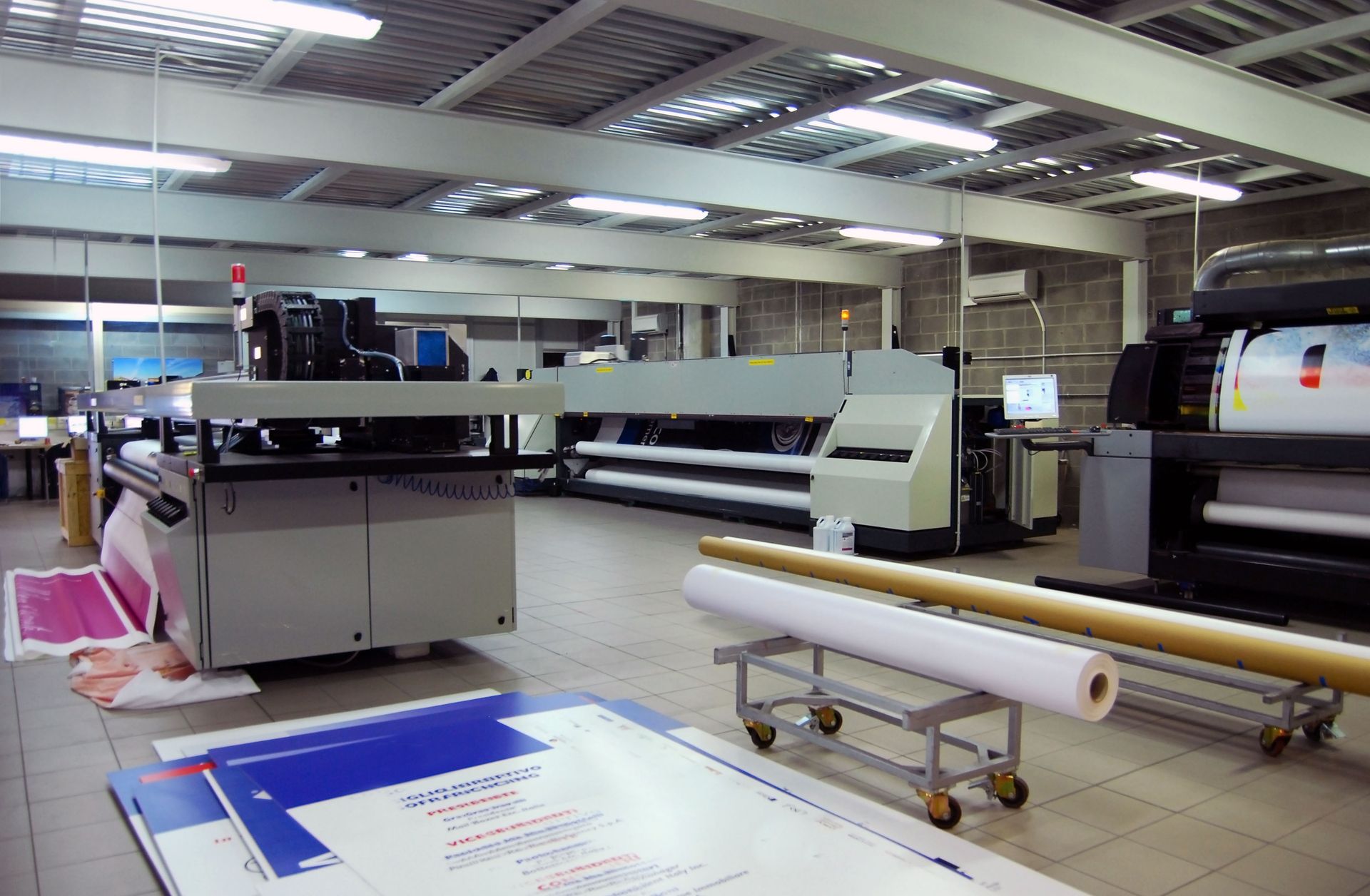 A printing factory interior with large printing machines, rolls of paper, and printed sheets.