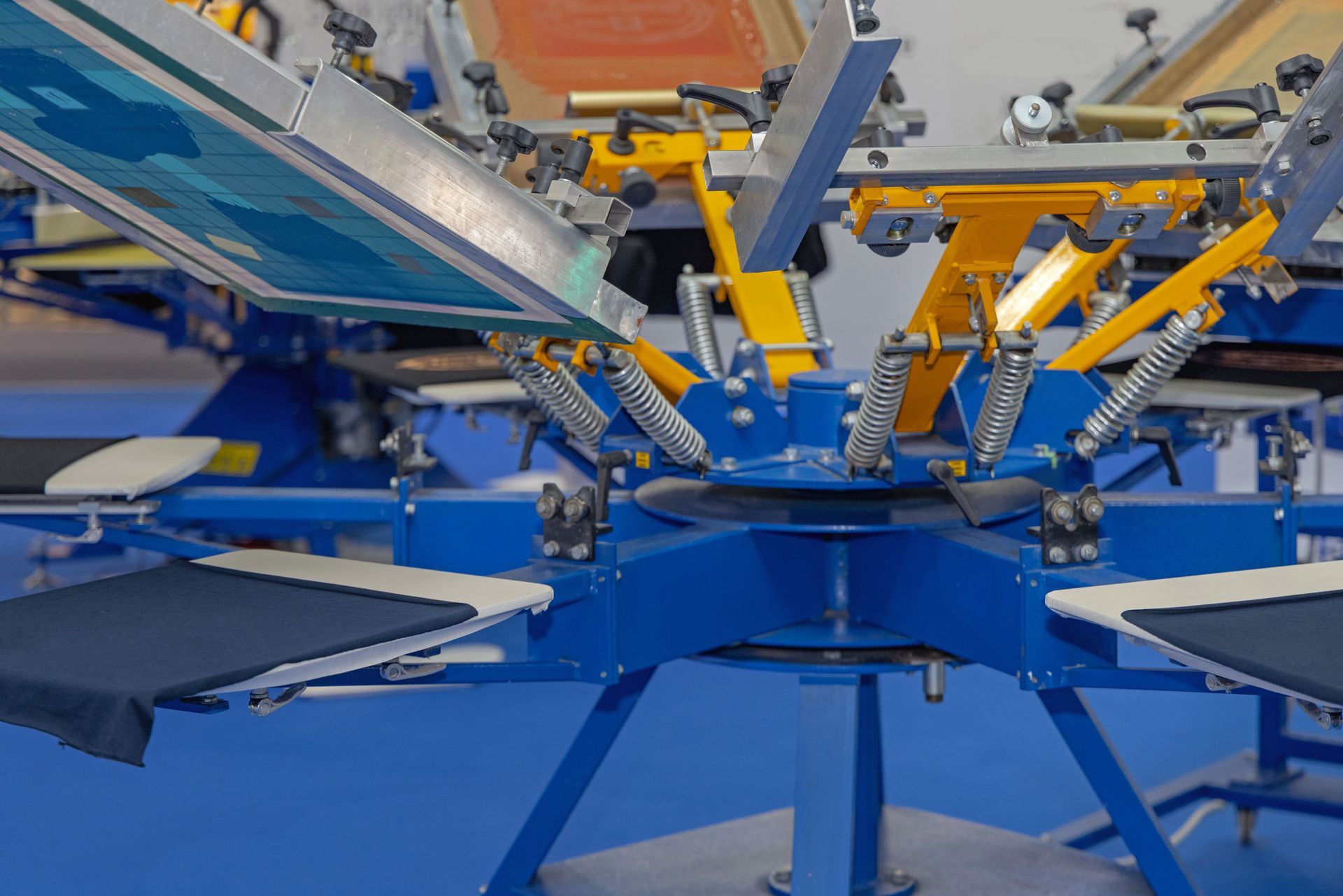 Blue and yellow screen printing machine with multiple arms and stations.