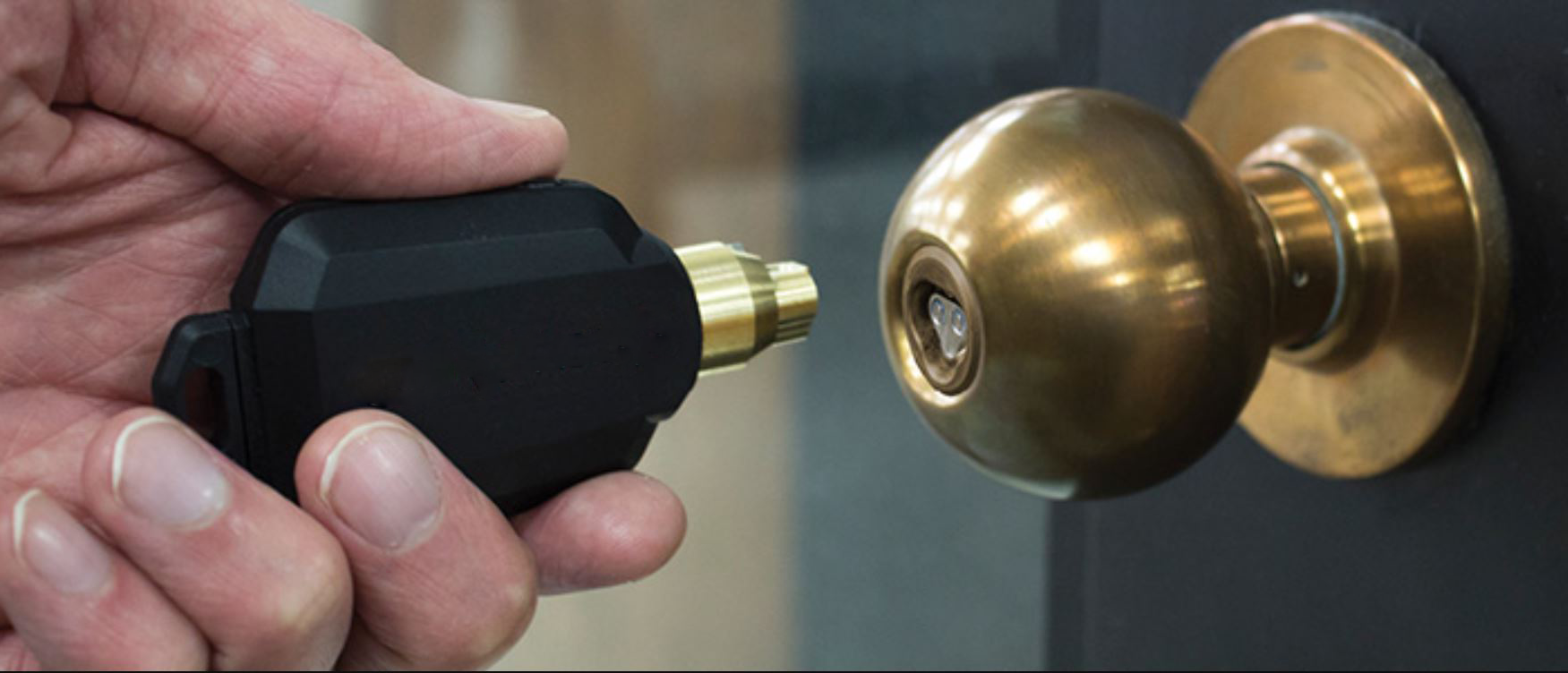 A person is holding a key next to a door knob.