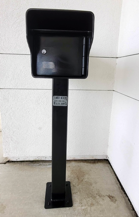 A black mailbox is sitting on top of a metal pole.