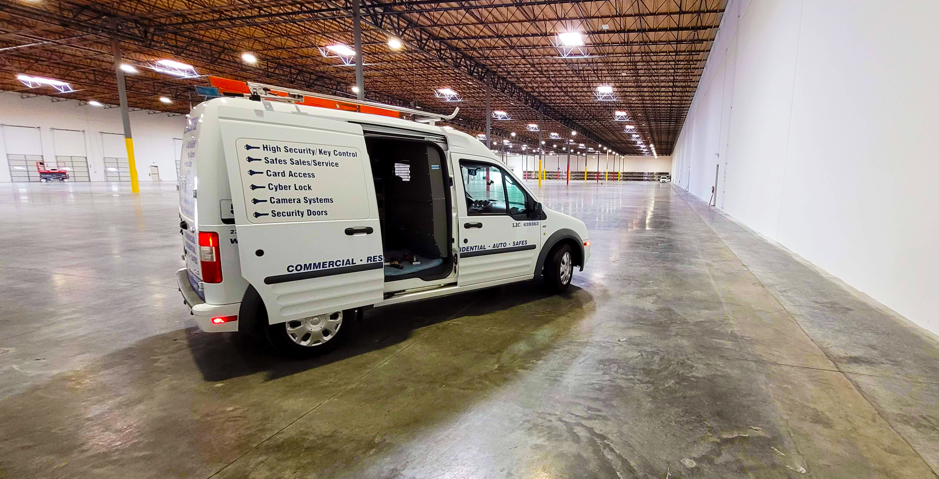A white van is parked in an empty warehouse with its doors open.