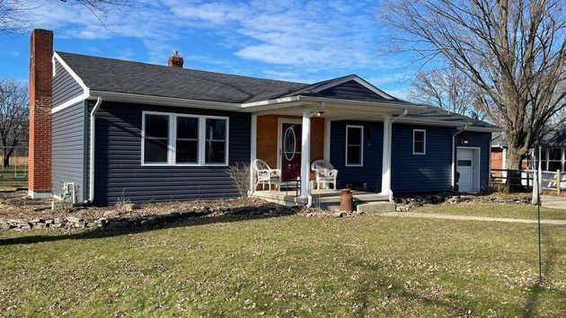 A single-story, dark blue house with a brick chimney and a white-columned front porch, set on a grassy lawn.