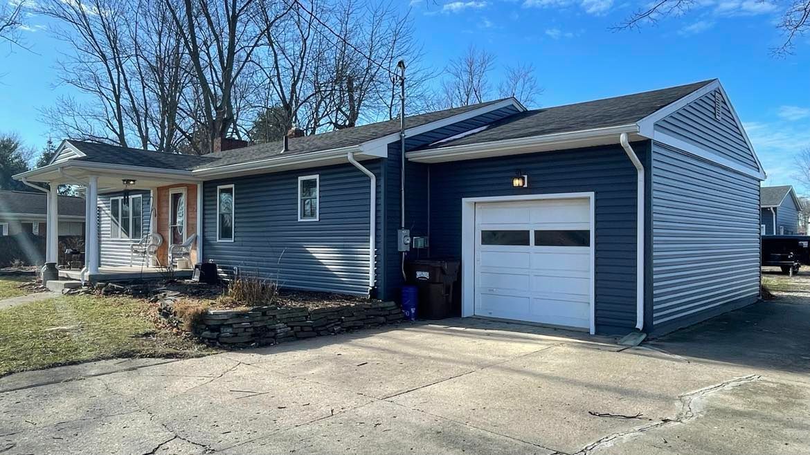 A blue, single-story house with a white front porch, matching trim, and an attached one-car garage on a sunny day.