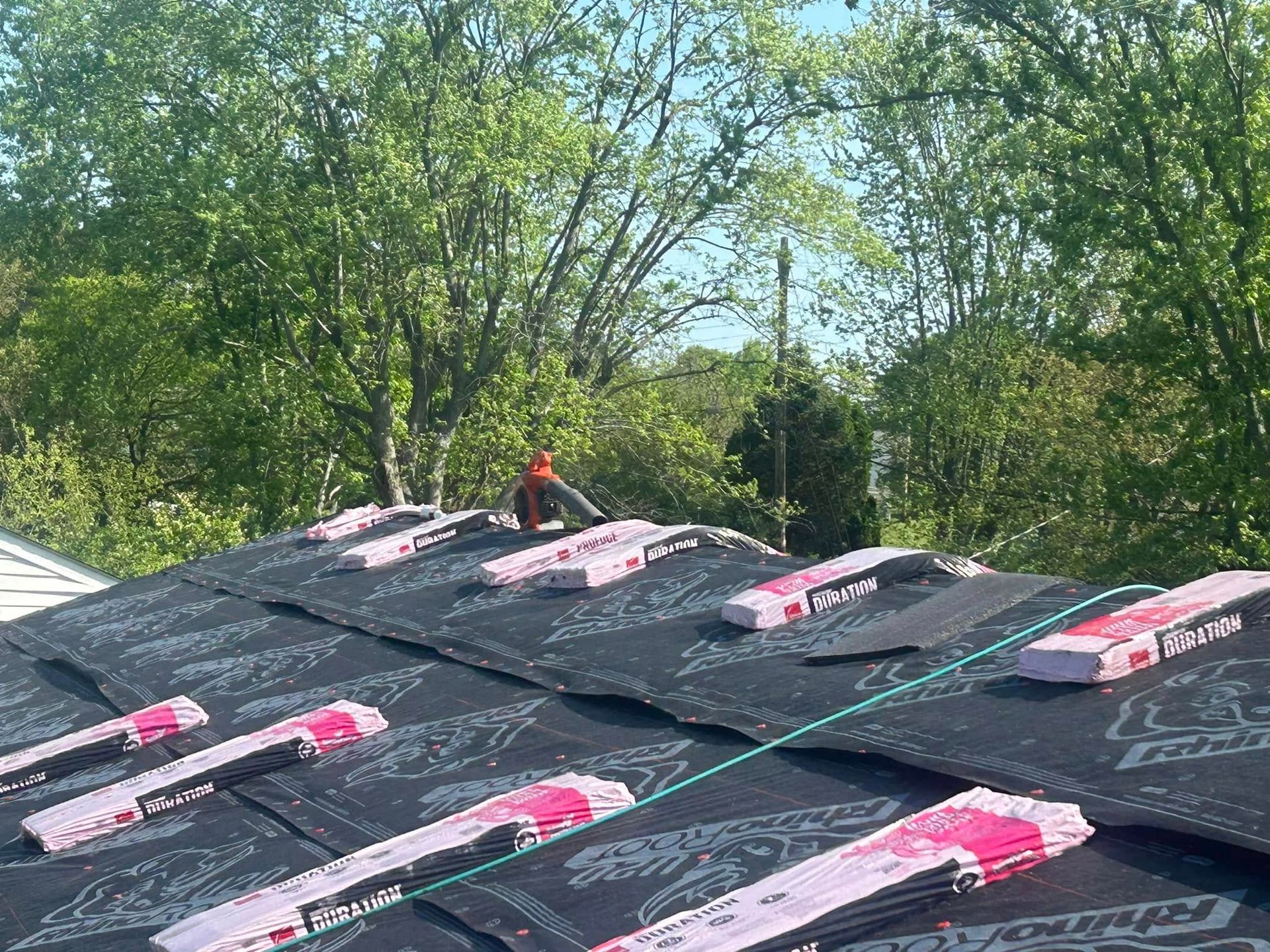 A roof under renovation, covered in black underlayment secured with pink-labeled fastener strips, viewed outdoors.