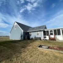 A two-story blue house with a white sunroom extension, surrounded by a large, dormant grass yard under a blue sky.
