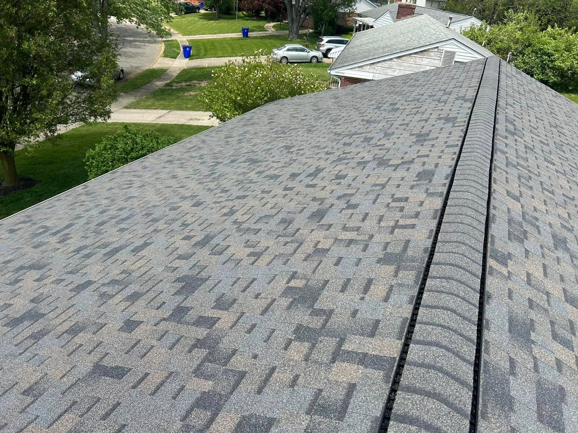 A high-angle view of a grey architectural asphalt shingle roof with a ridge cap running along the peak.
