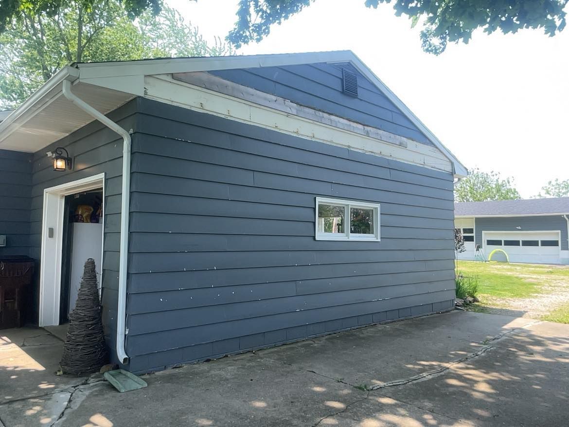 A side view of a dark gray garage with white trim, a single rectangular window, and a white side door under a light.
