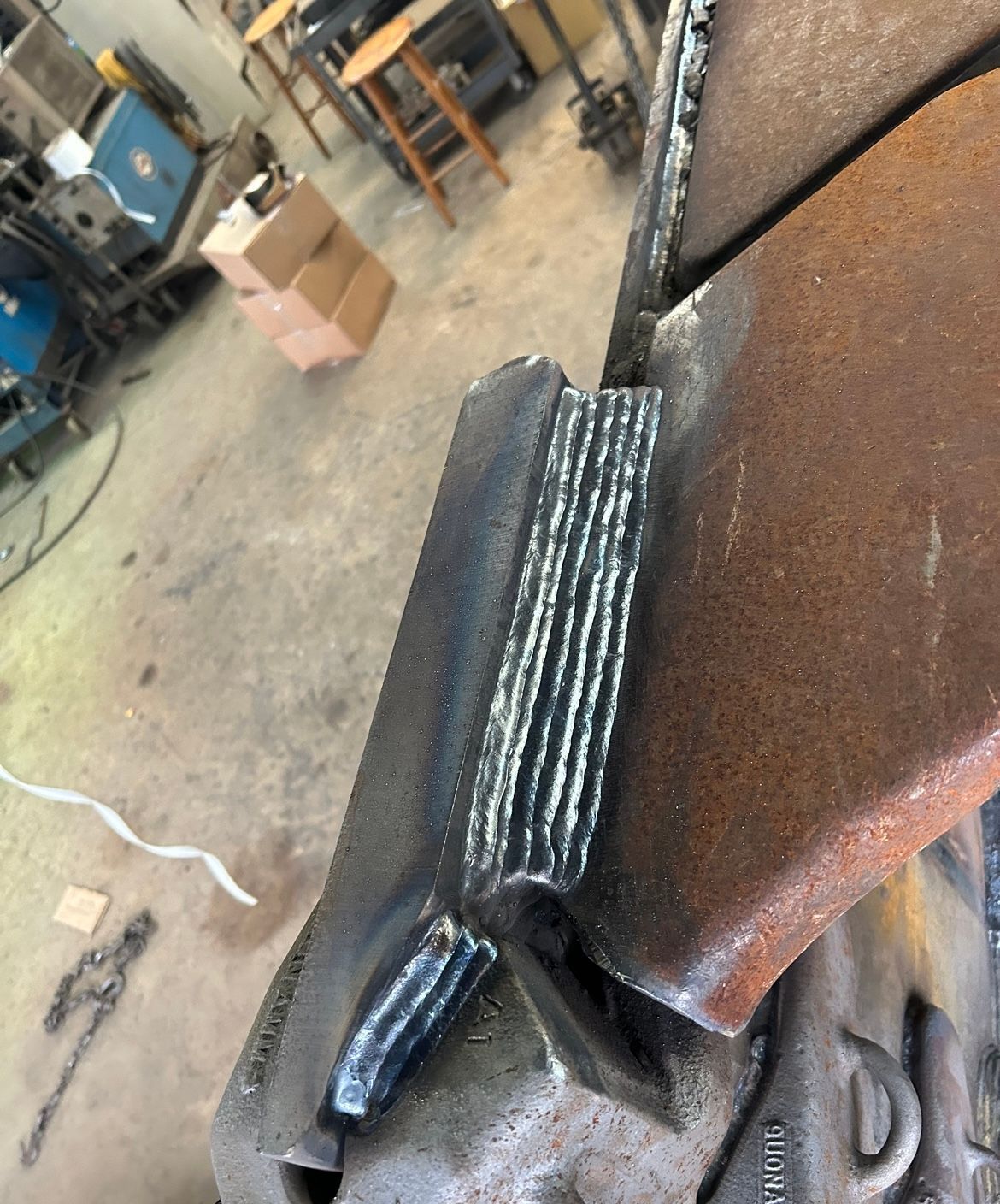 Close-up of a metal welding joint. Vertical welds connect two steel plates in a workshop setting.
