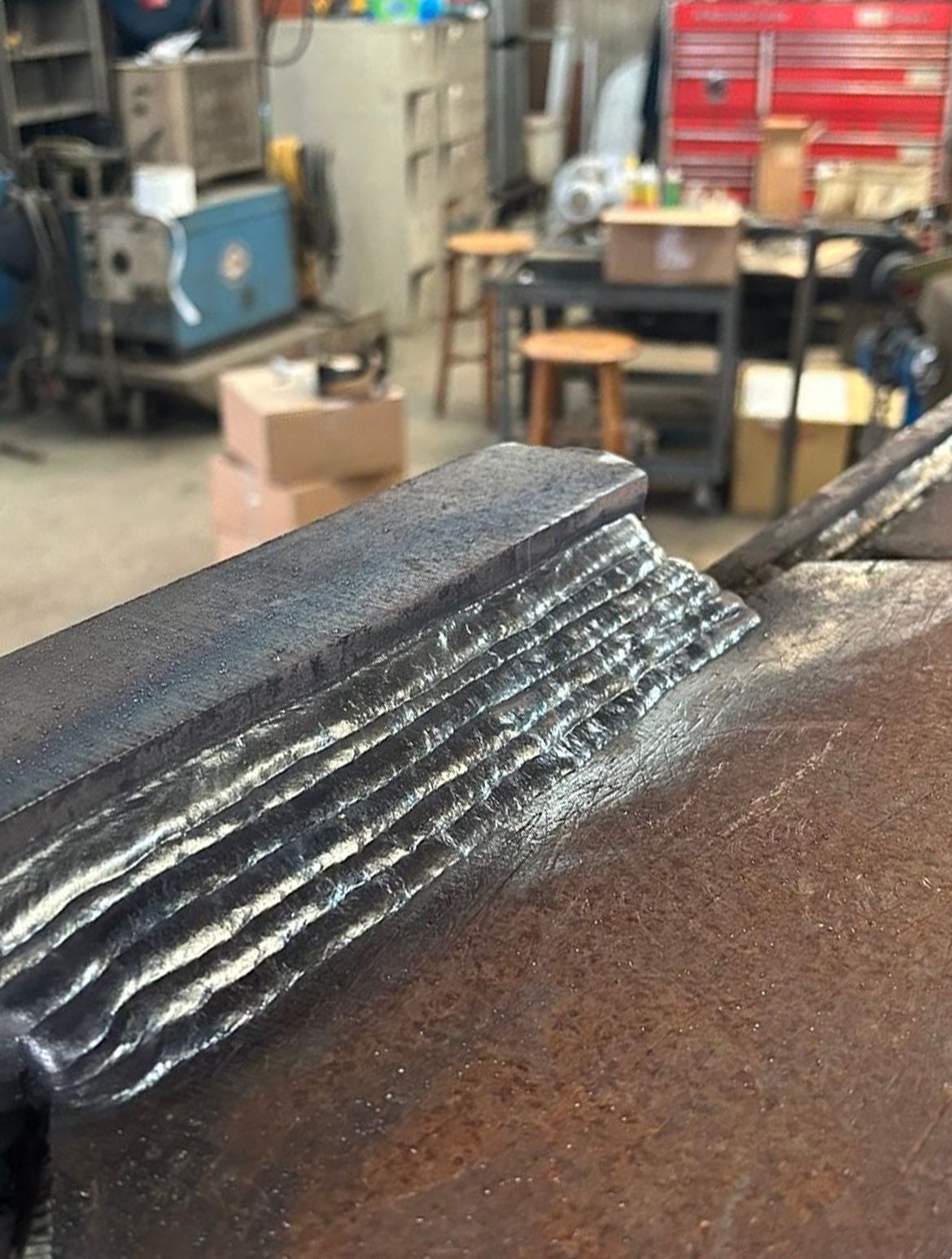 Close-up of a stack of metal plates welded together, clamped in a vise in a workshop setting.
