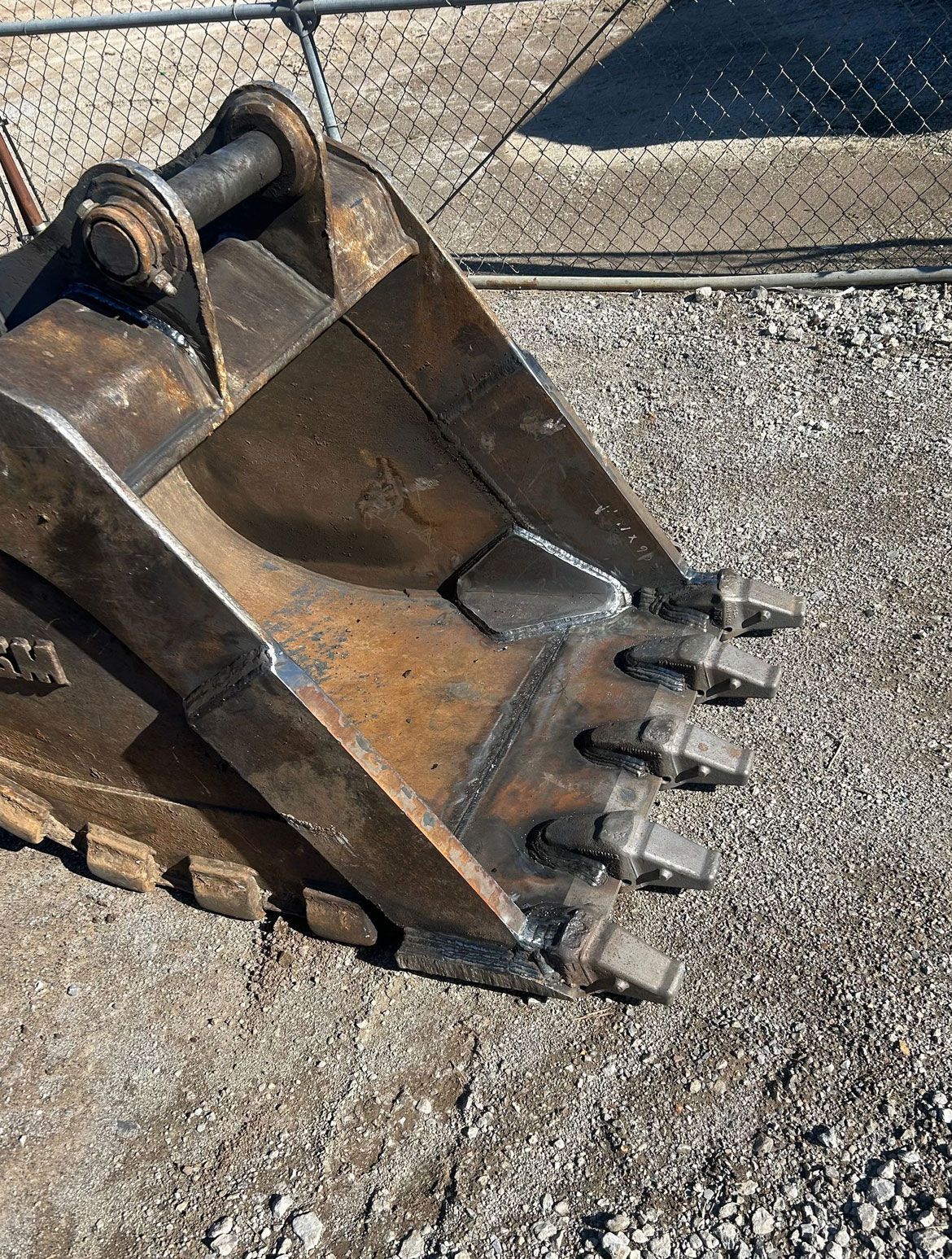 Excavator bucket with teeth, outdoors on gravel.