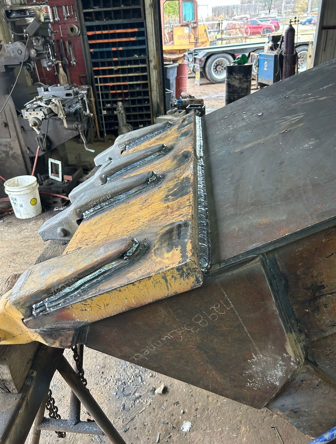 A large metal industrial piece, possibly a bucket, being welded in a workshop setting.