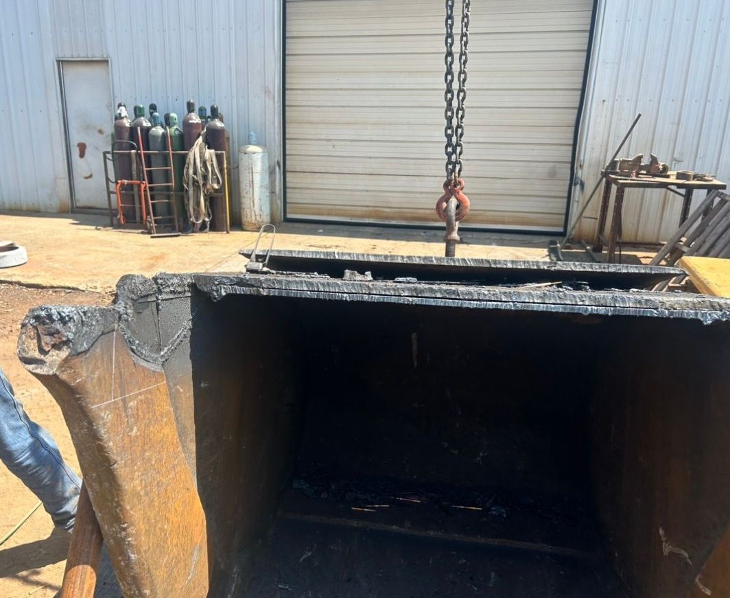 Large, open metal container being lifted by a chain, likely in a warehouse setting.