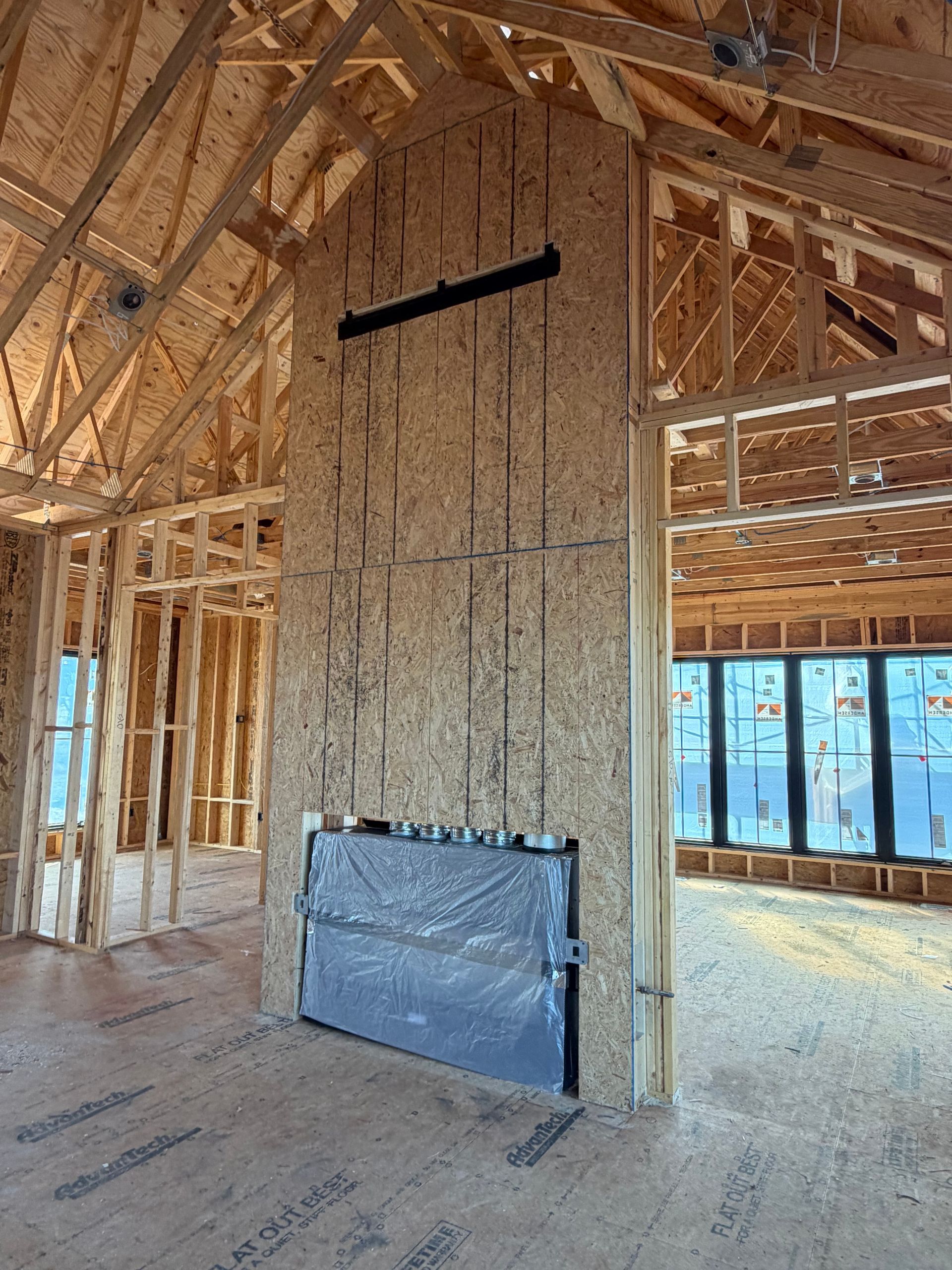 Unfinished house interior with a tall brick fireplace and exposed wood framing under construction.