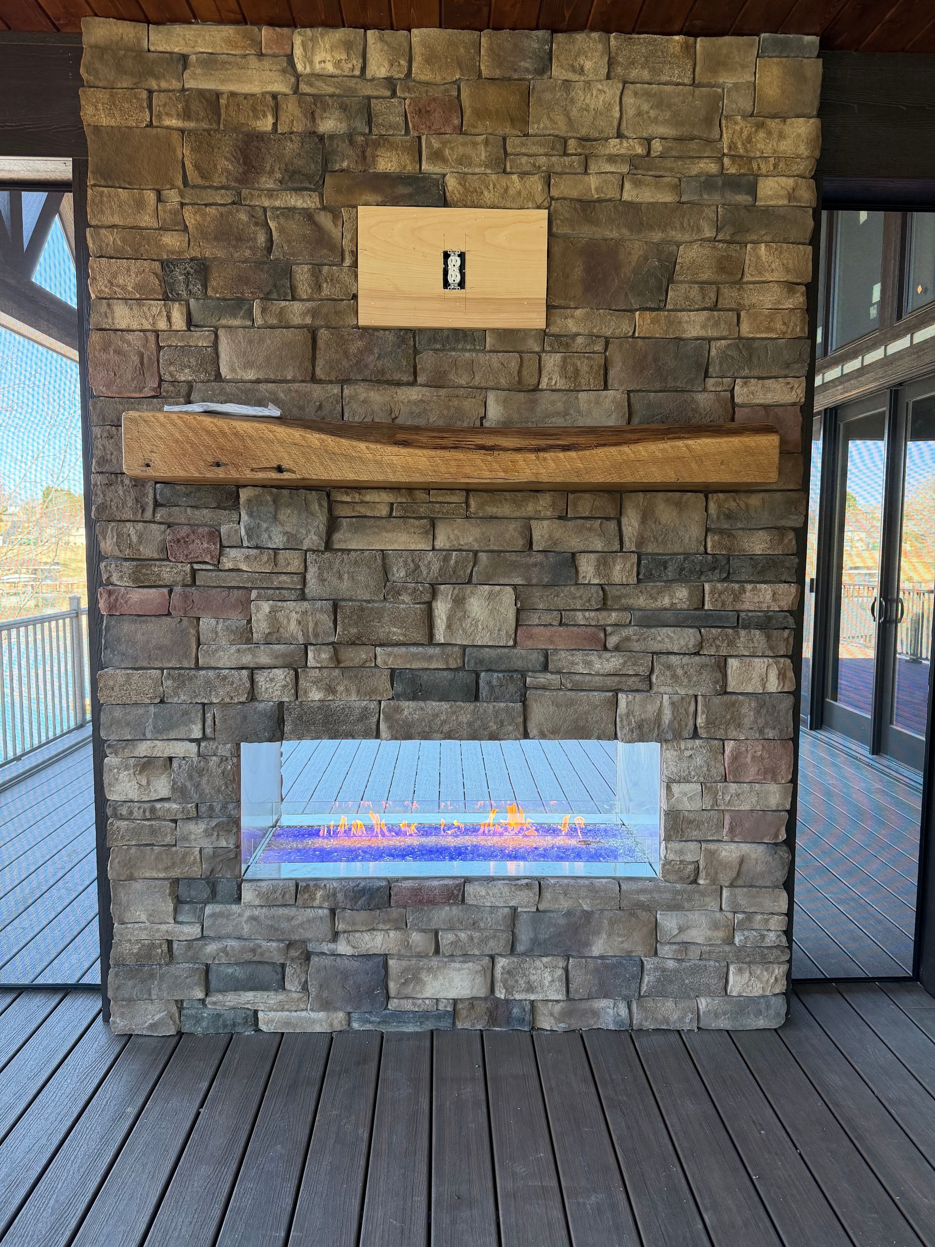 Stone wall with a wooden ledge and two signs on an outdoor deck by a railing.