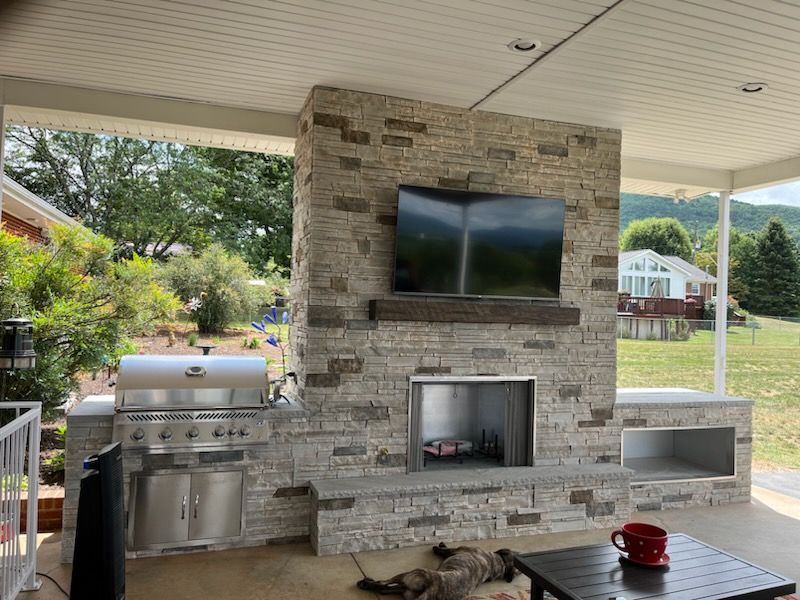 Covered patio with stone fireplace, wall-mounted TV, grill, and red kettle on a table
