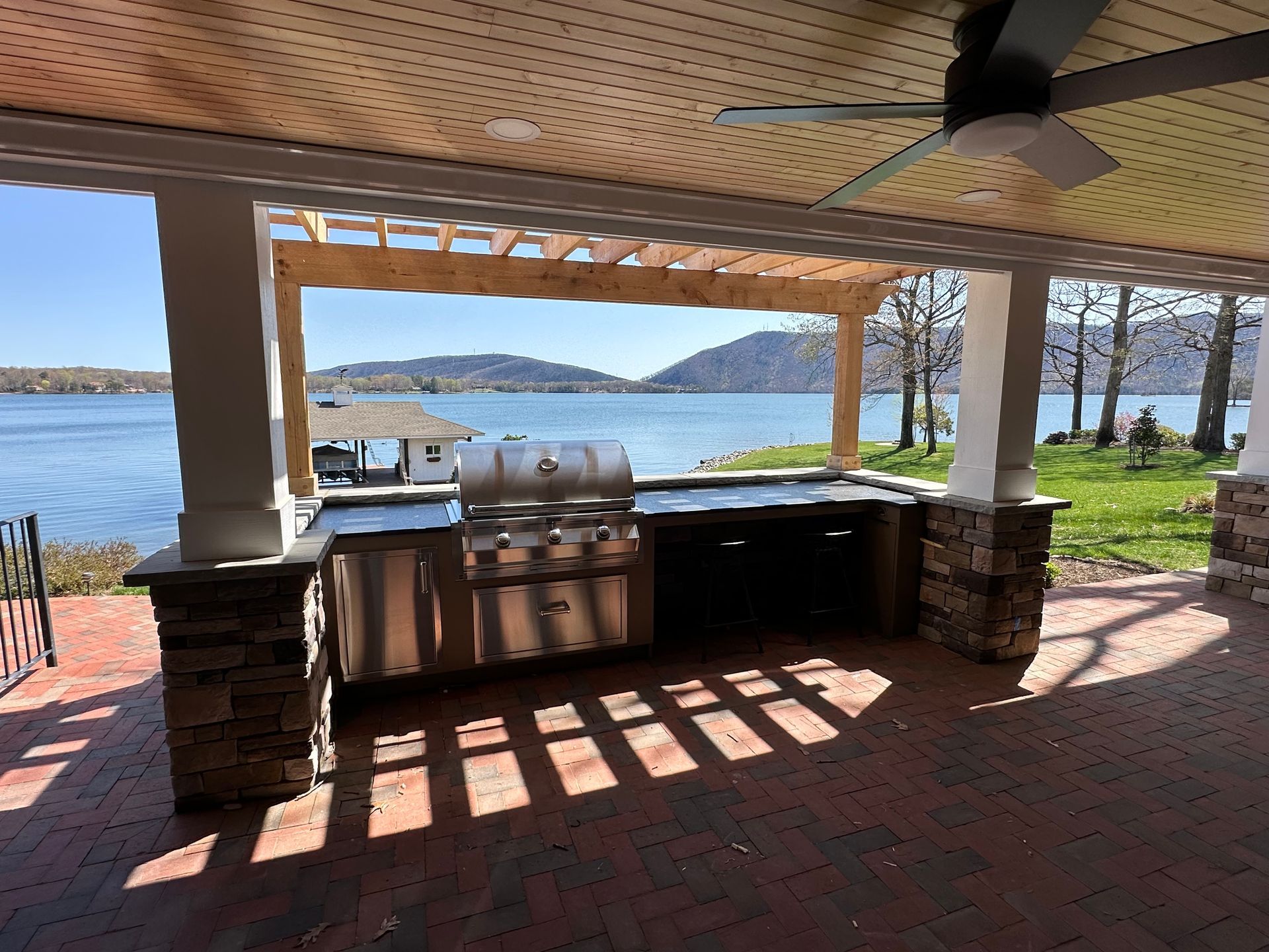 Lakefront patio with covered grill, wooden bar, and view of water and distant hills