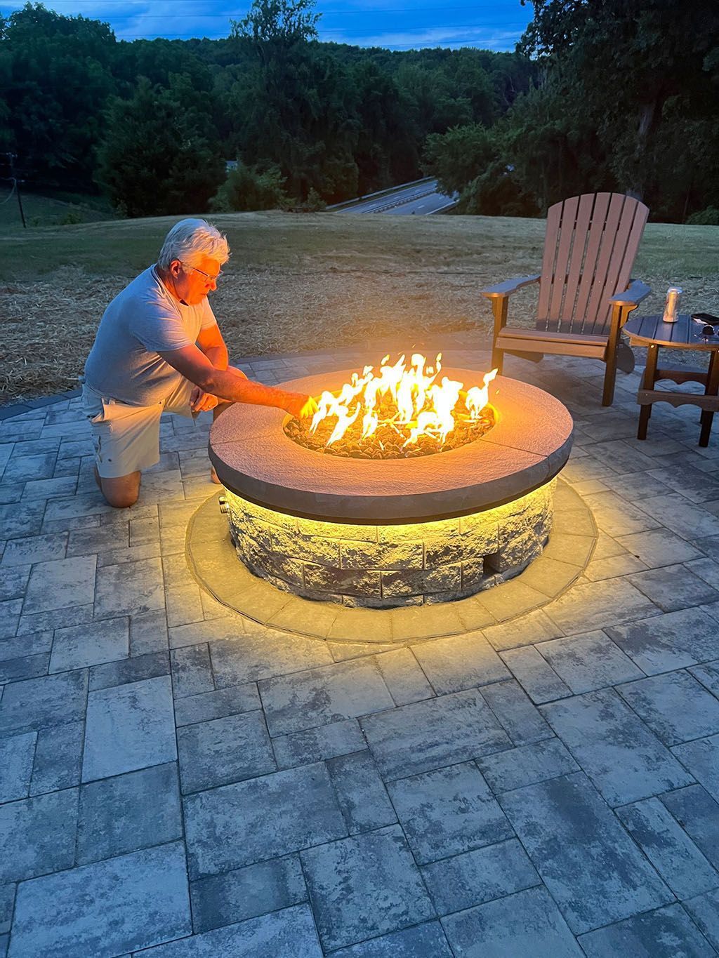 Person lighting a round fire pit in a backyard patio at dusk
