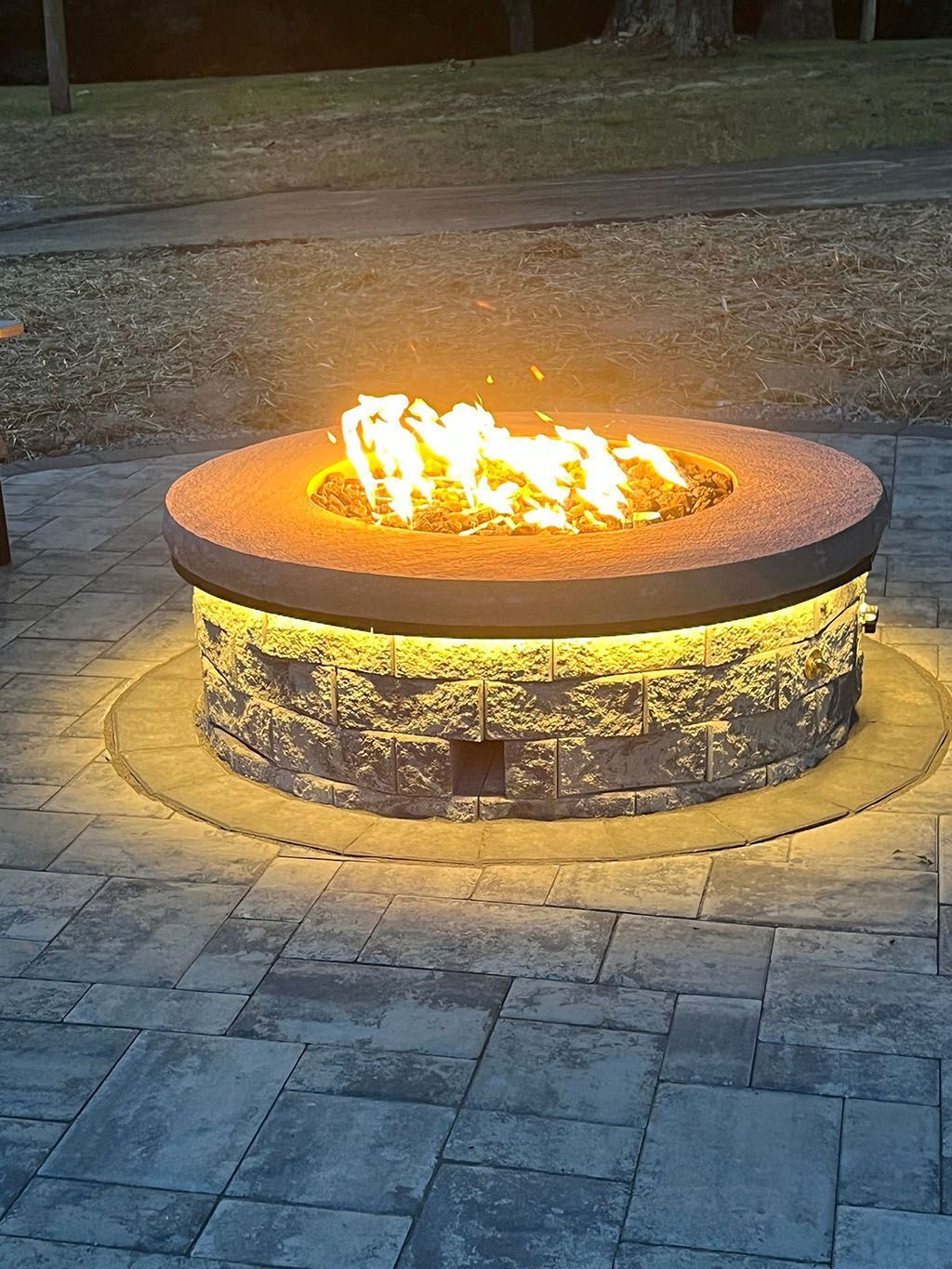 Round stone fire pit with bright flames glowing in a paved outdoor area