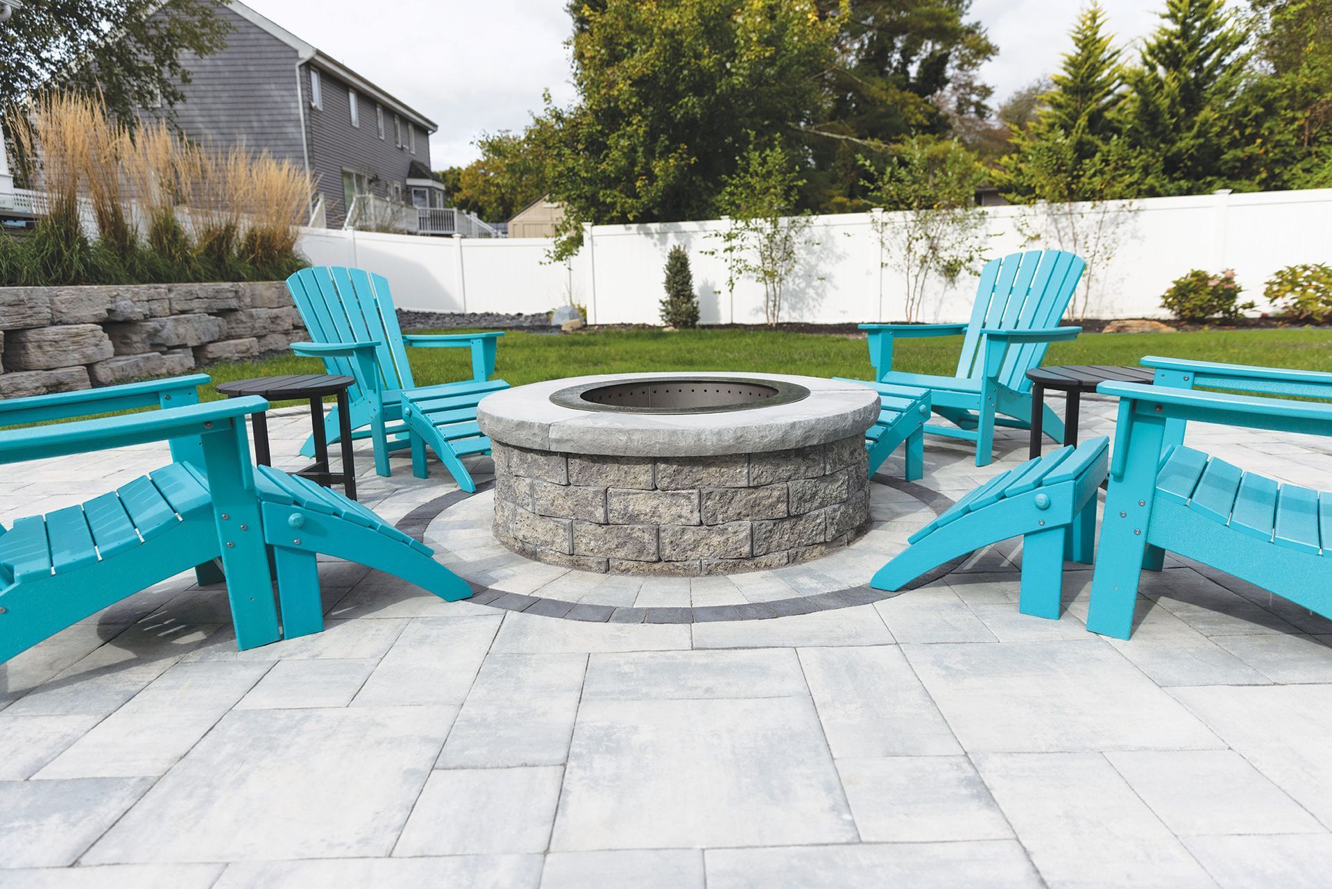 Blue patio chairs around a stone fire pit on a tiled backyard patio