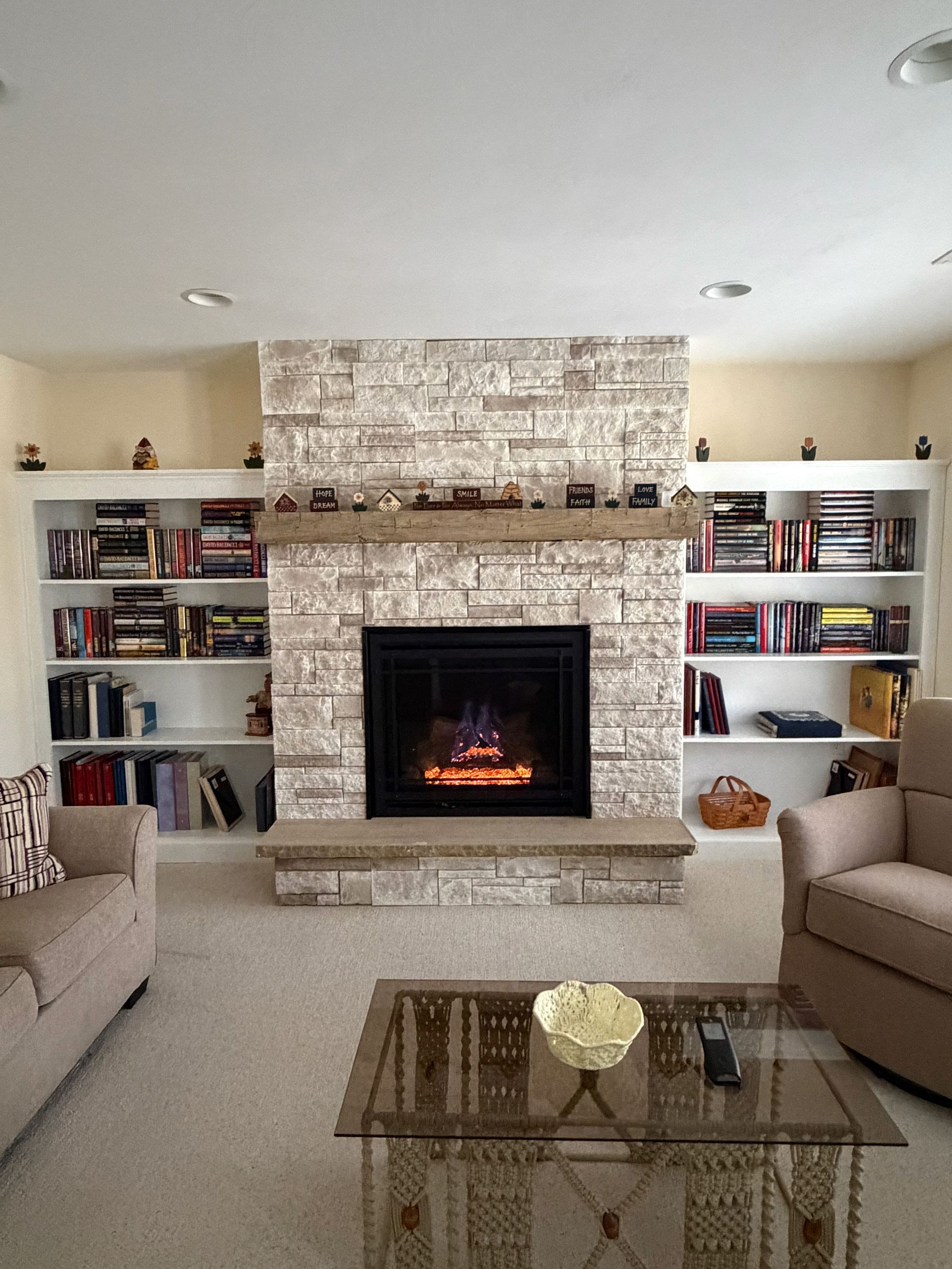 Living room with brick fireplace, built-in shelves, beige sofas, and a glass coffee table.