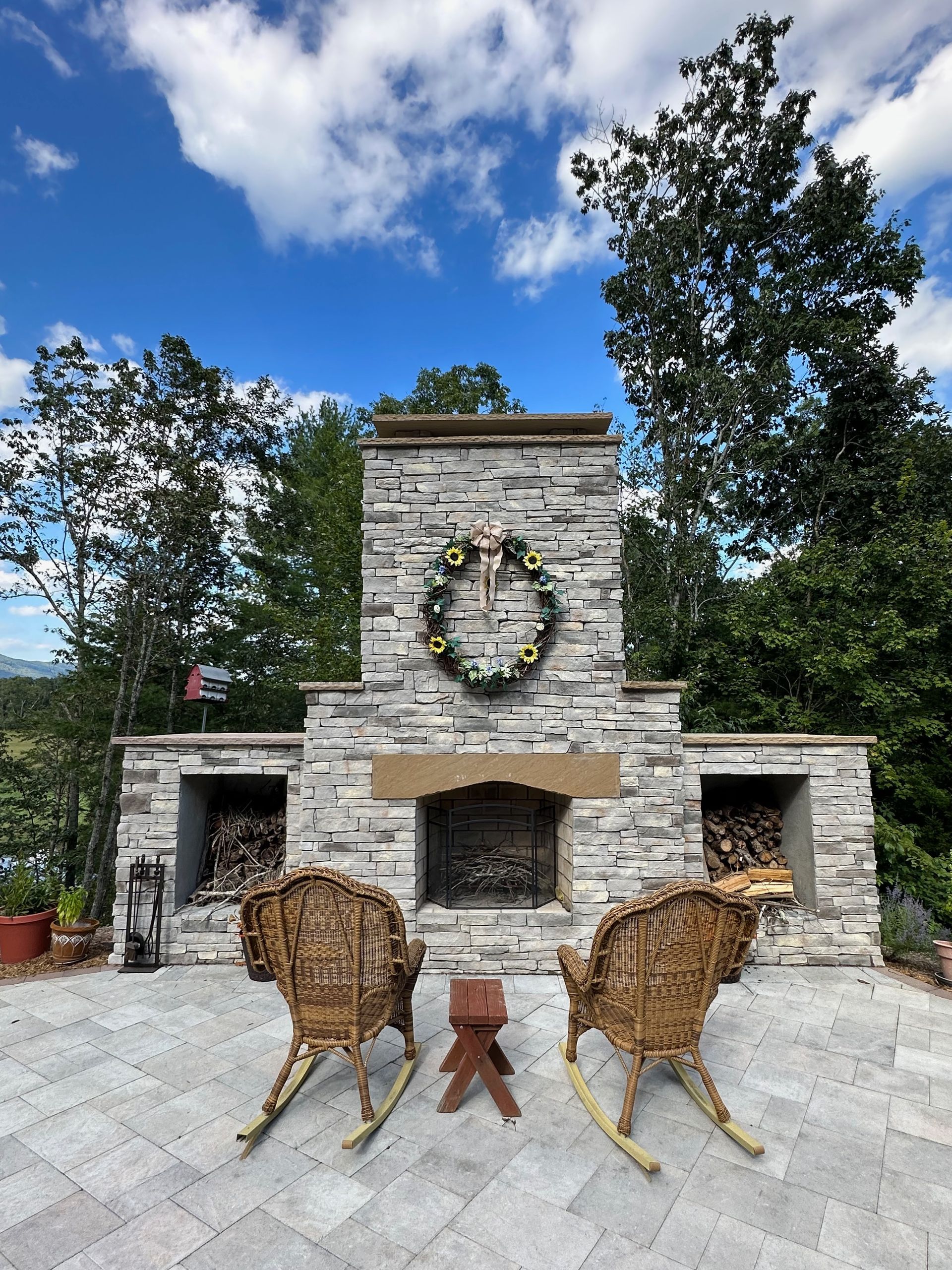 Stone outdoor fireplace with wreath, framed by two metal deer sculptures under a blue sky.