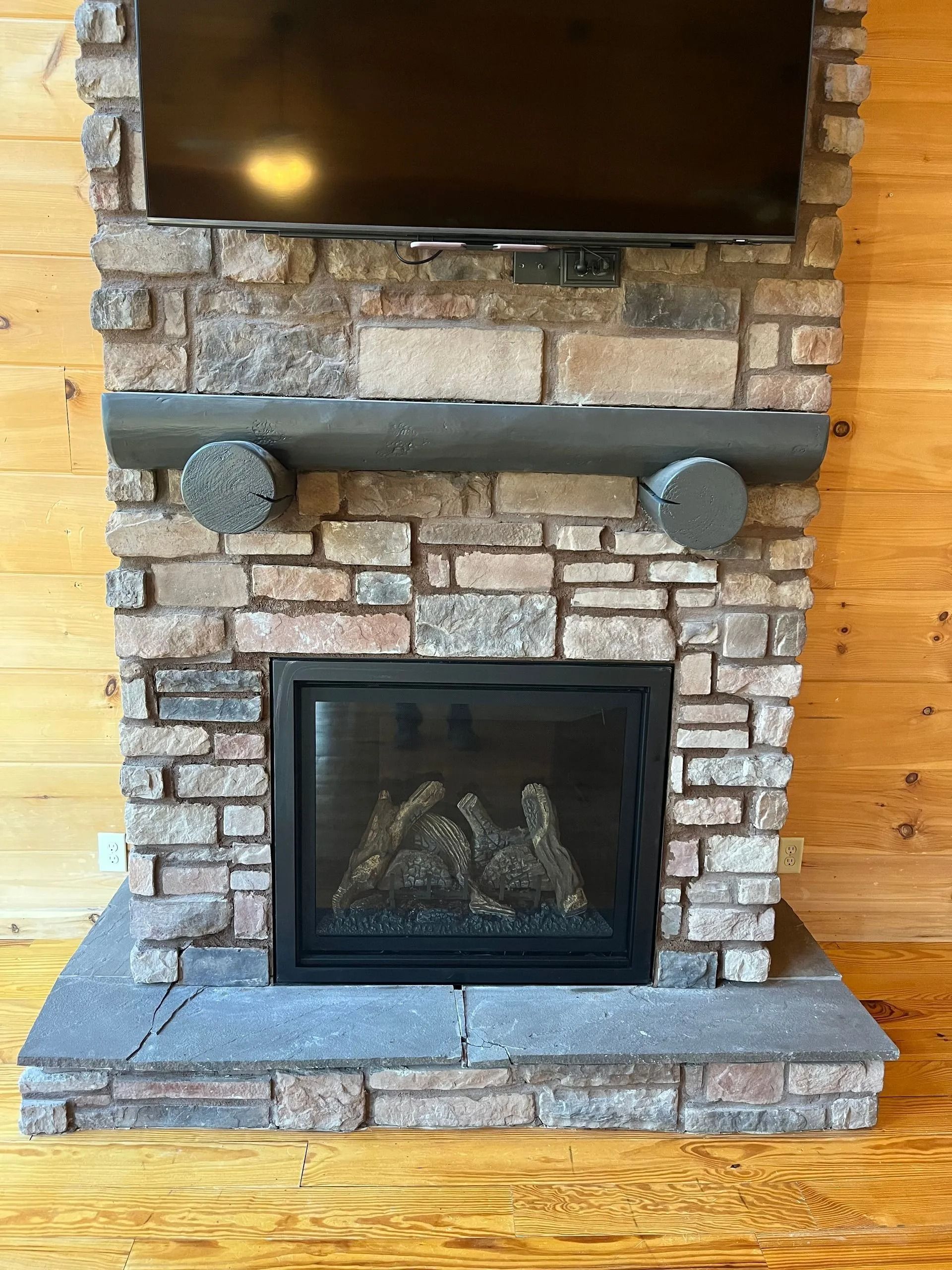 Stone fireplace with TV above, gas fireplace insert, wooden paneling.