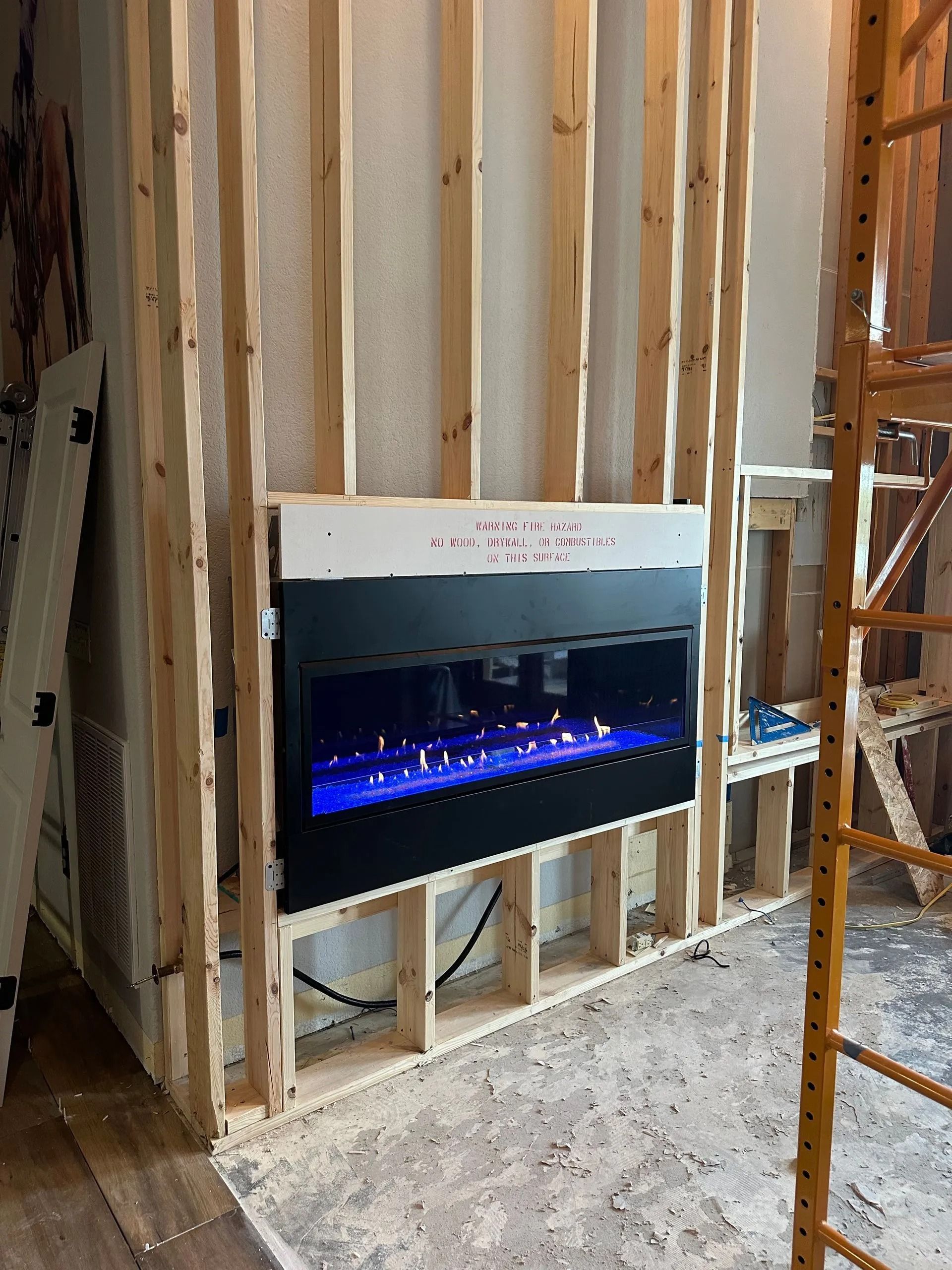 Electric fireplace installed in a wooden frame during renovation. Blue flames visible.