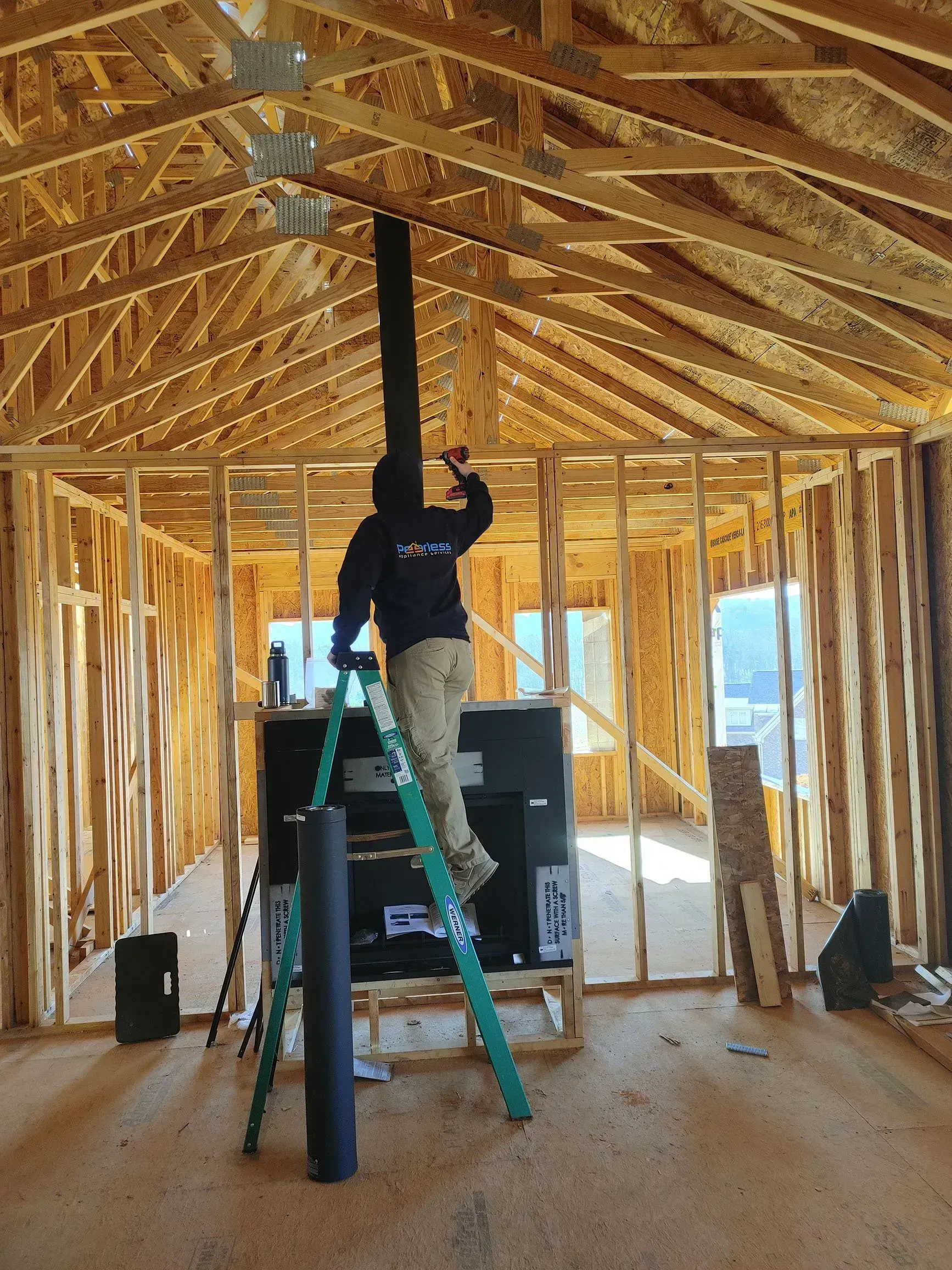 Man on ladder installing HVAC ductwork in a new home construction. Wooden framing is visible.