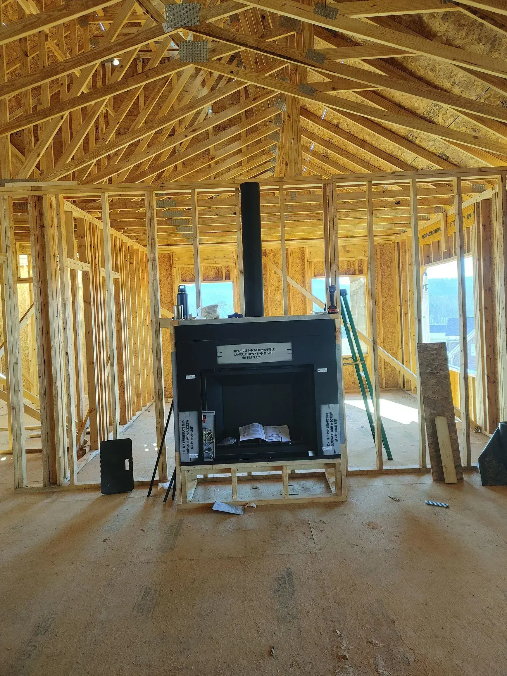 Interior framing of a house under construction with a black fireplace and chimney.