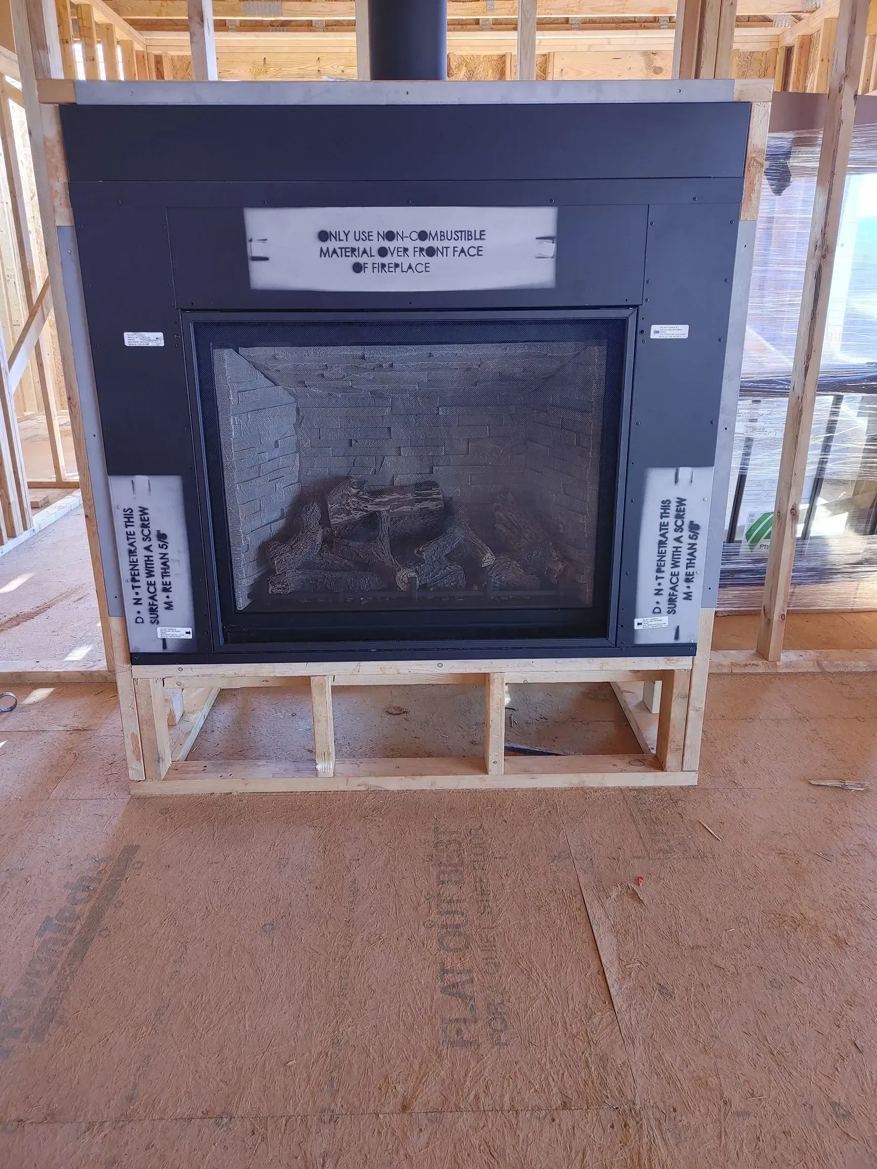 A fireplace in a wooden frame during construction, with a dark gray metal face and chimney.
