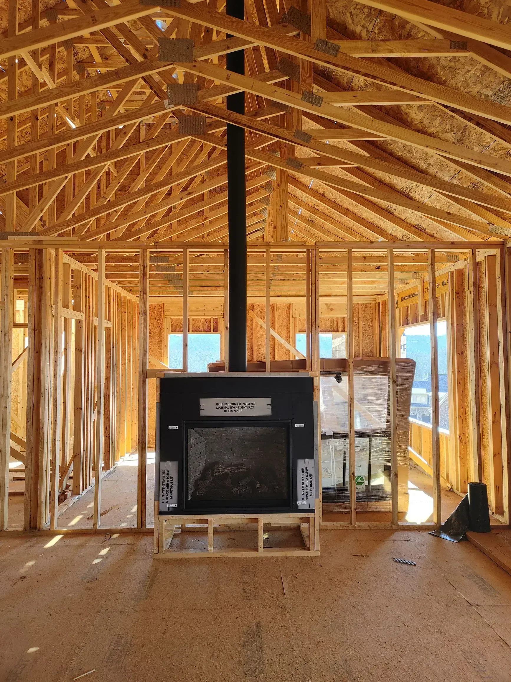 Interior of a house under construction; a fireplace with black chimney is centered in the wooden frame.